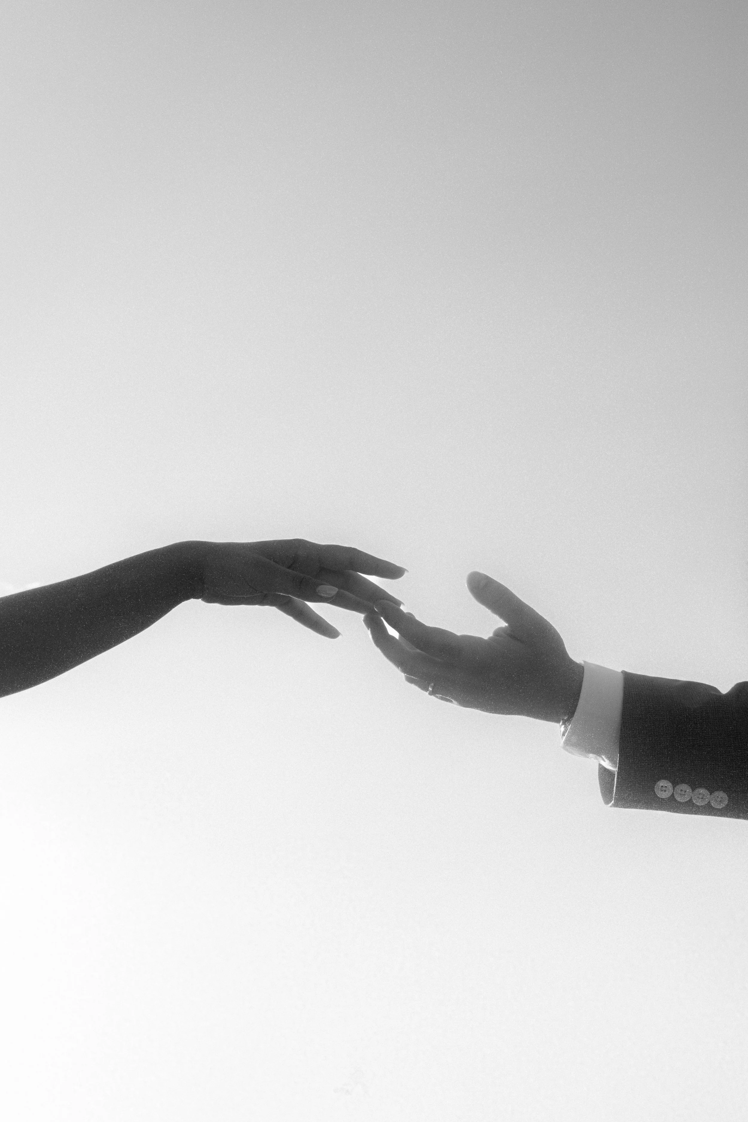 Deux mains se touchant, dont une habillée en costume et l'autre nue, dans une image en noir et blanc.