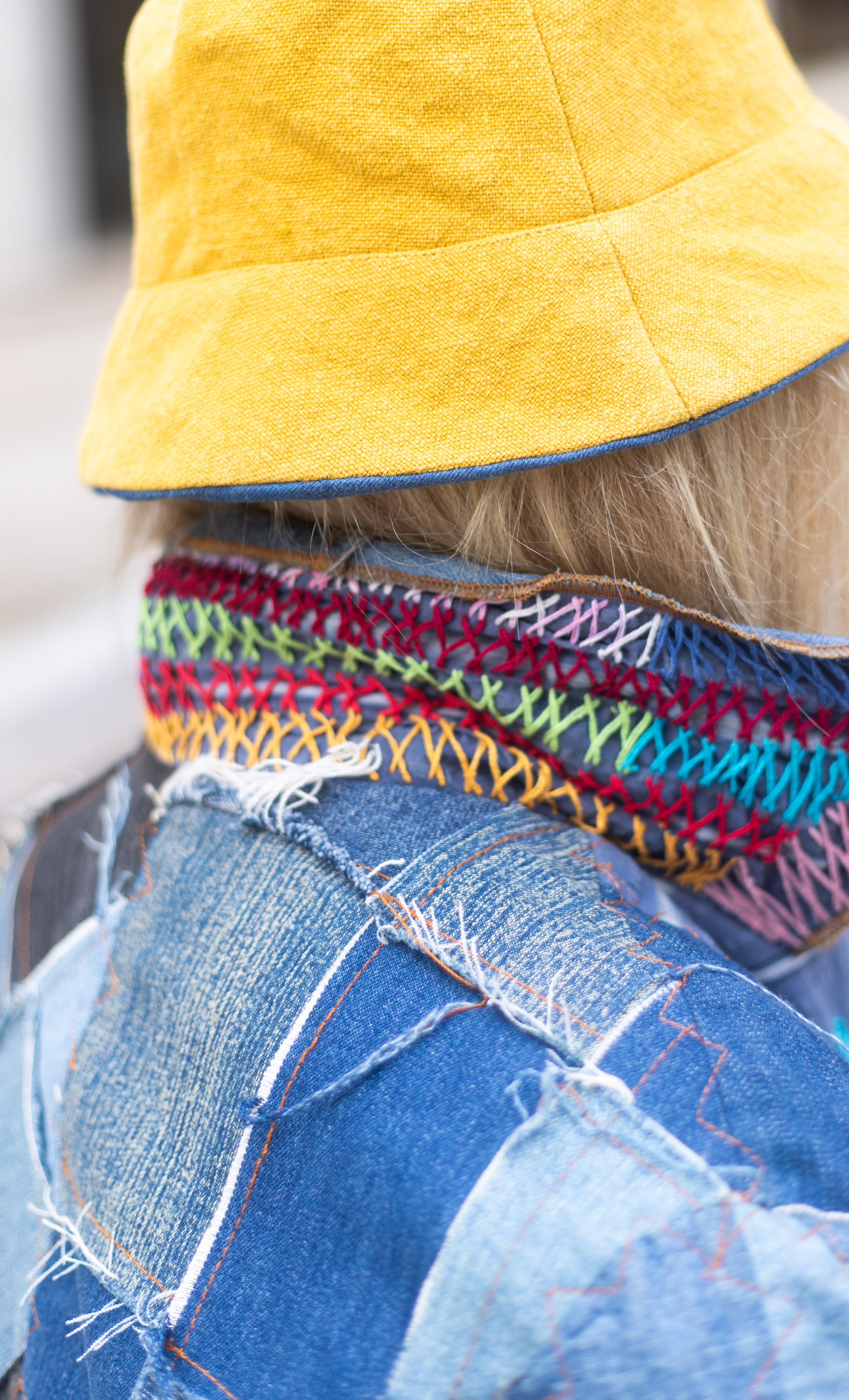 Une personne portant un bonnet jaune en tissu, une écharpe multicolore en crochet et un jean déchiré.