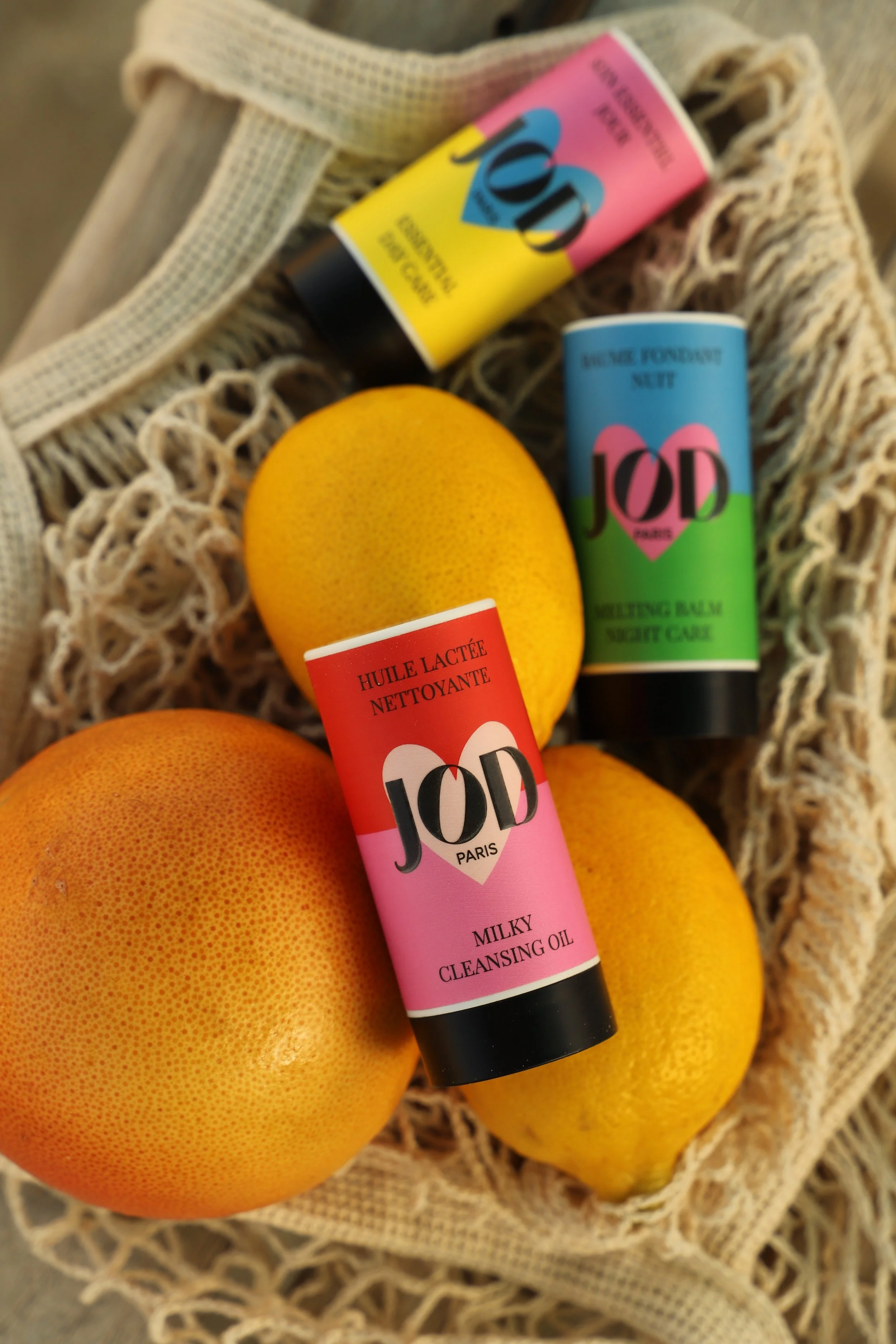 Pommes grapefruit et trois tubes de soins de la marque JOD, dont un nettoyant, un baume de nuit et un huile nettoyante, disposés dans un panier en tissu.