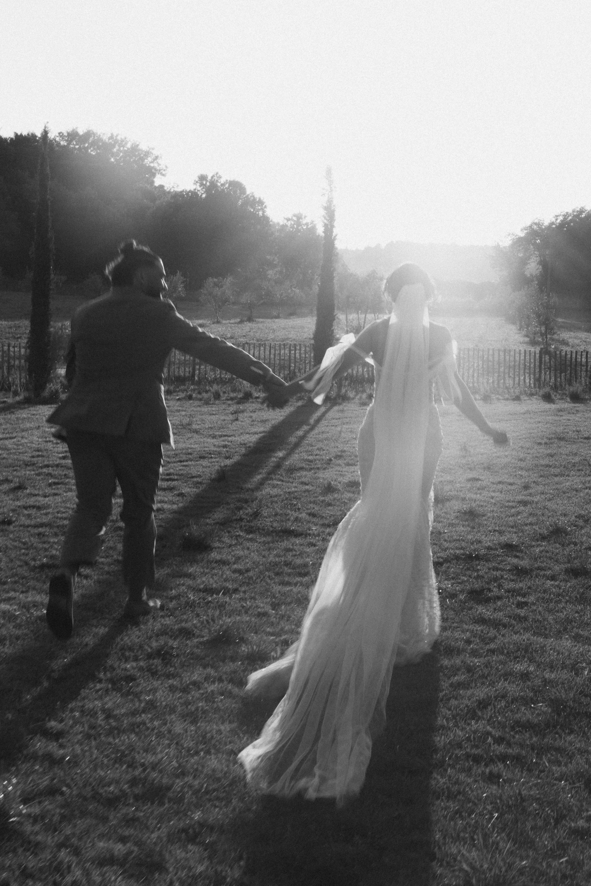 Un couple en mariage danse dans un champ en plein air au coucher du soleil.
