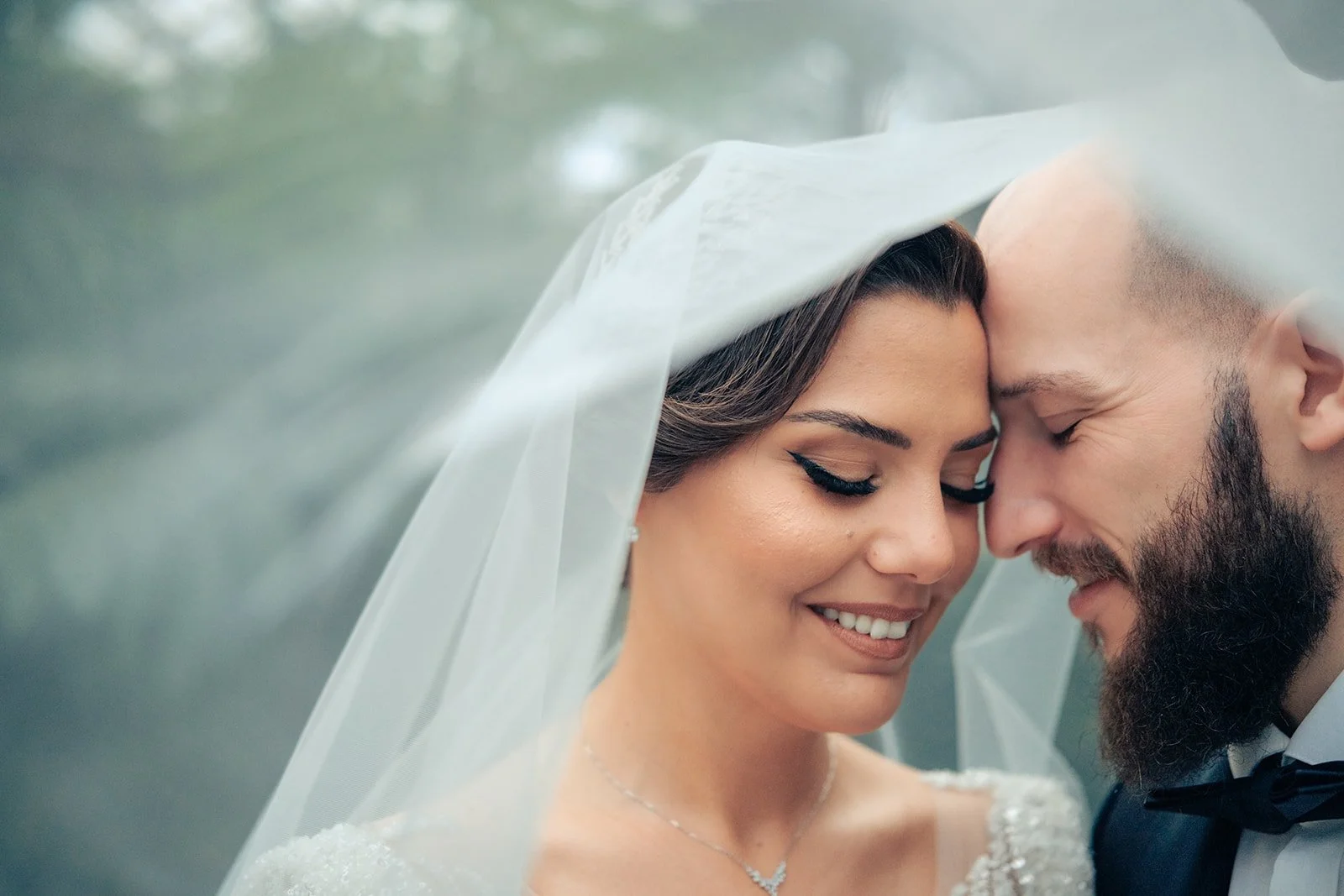 eune mariée et son époux, souriants et complices, sous le voile de la mariée lors d’une séance photo intimiste et naturelle.