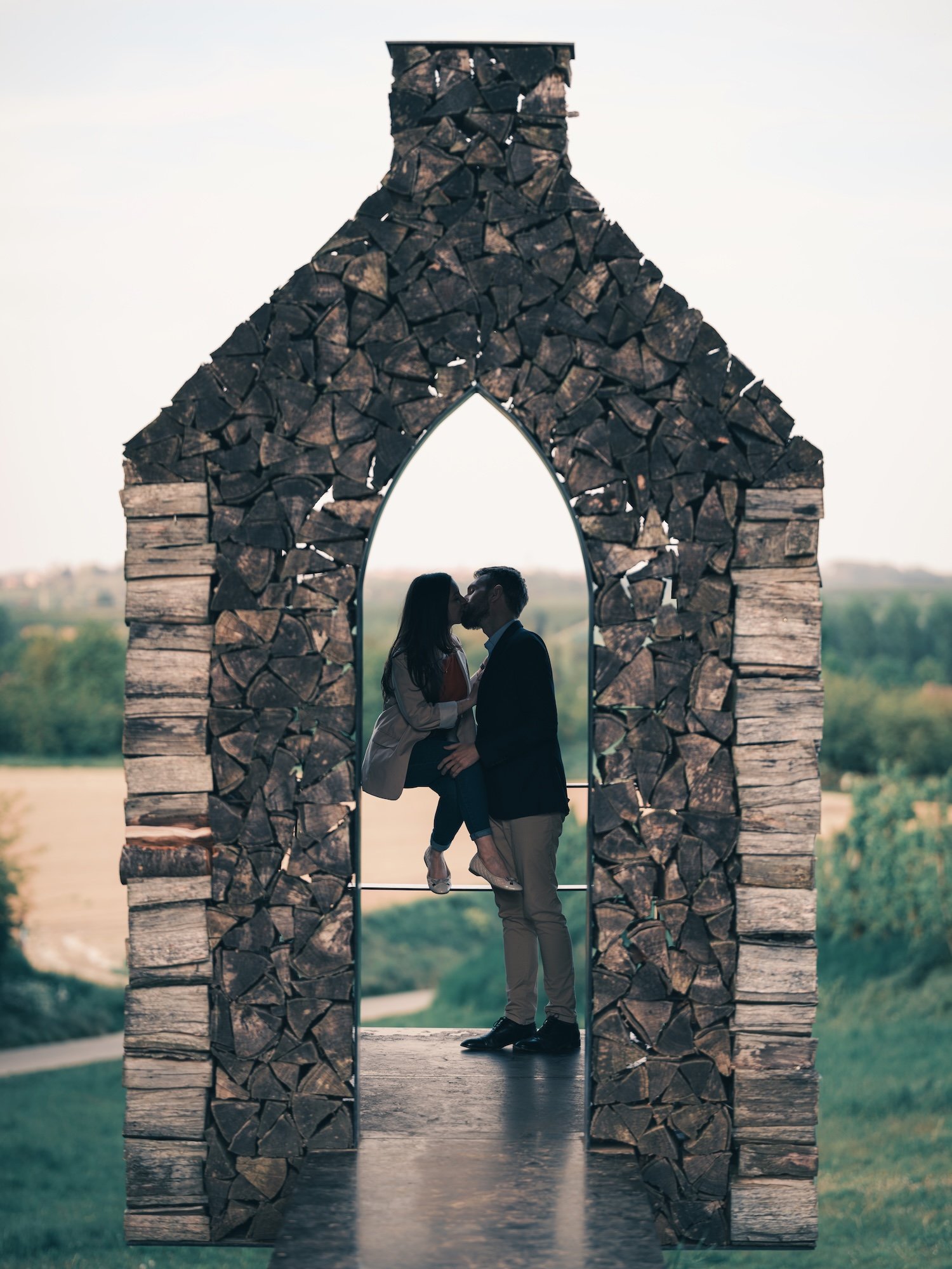 Couple qui s'embrasse dans une arche de bûches empilées, avec vue sur la campagne