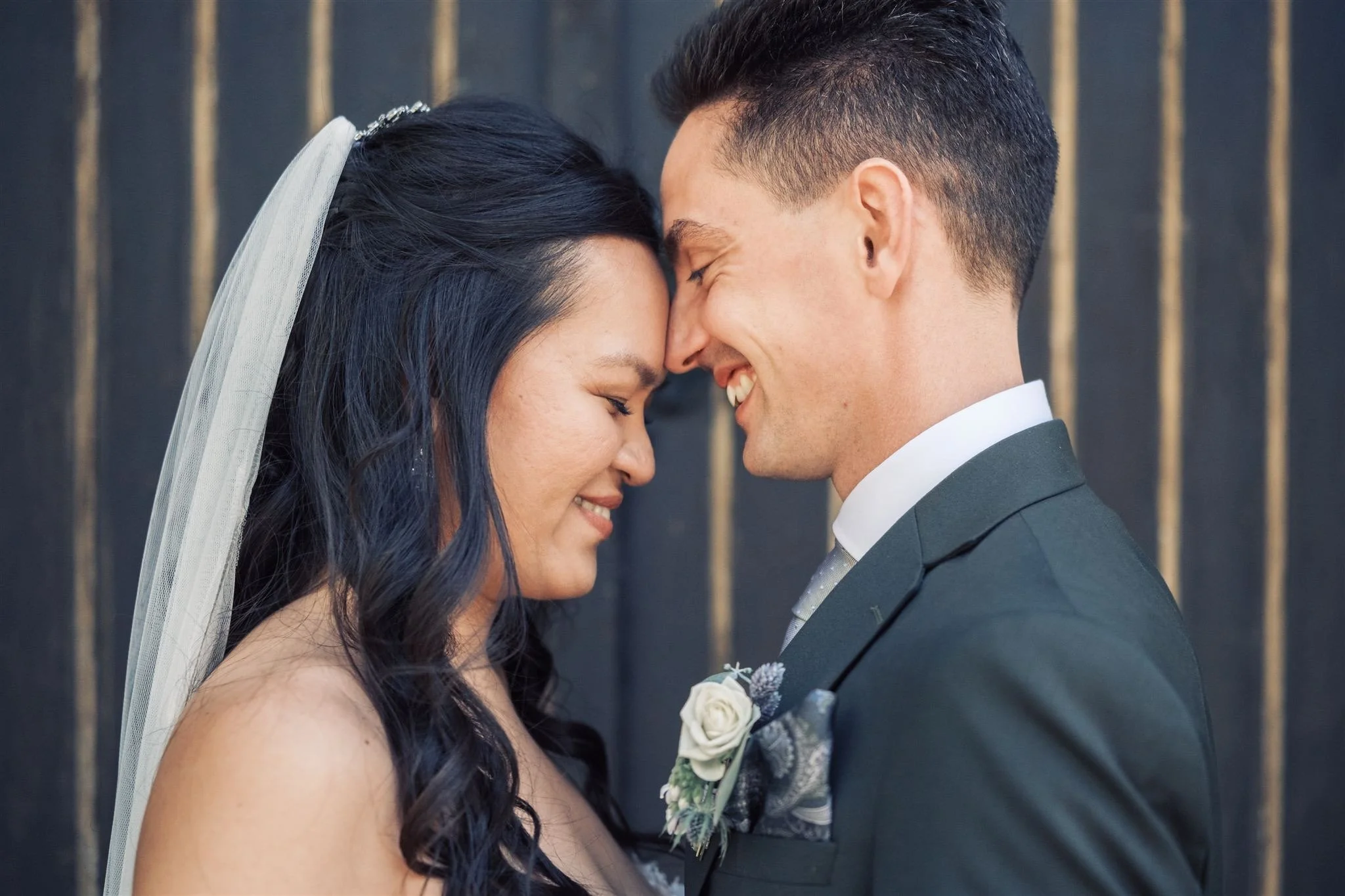 Photographe de mariage capturant l'instant complice d'un couple de mariés — voile blanc, costume gris et boutonnière fleurie — dans un portrait intime et lumineux, symbole d'une photographie de mariage naturelle et émotionnelle.