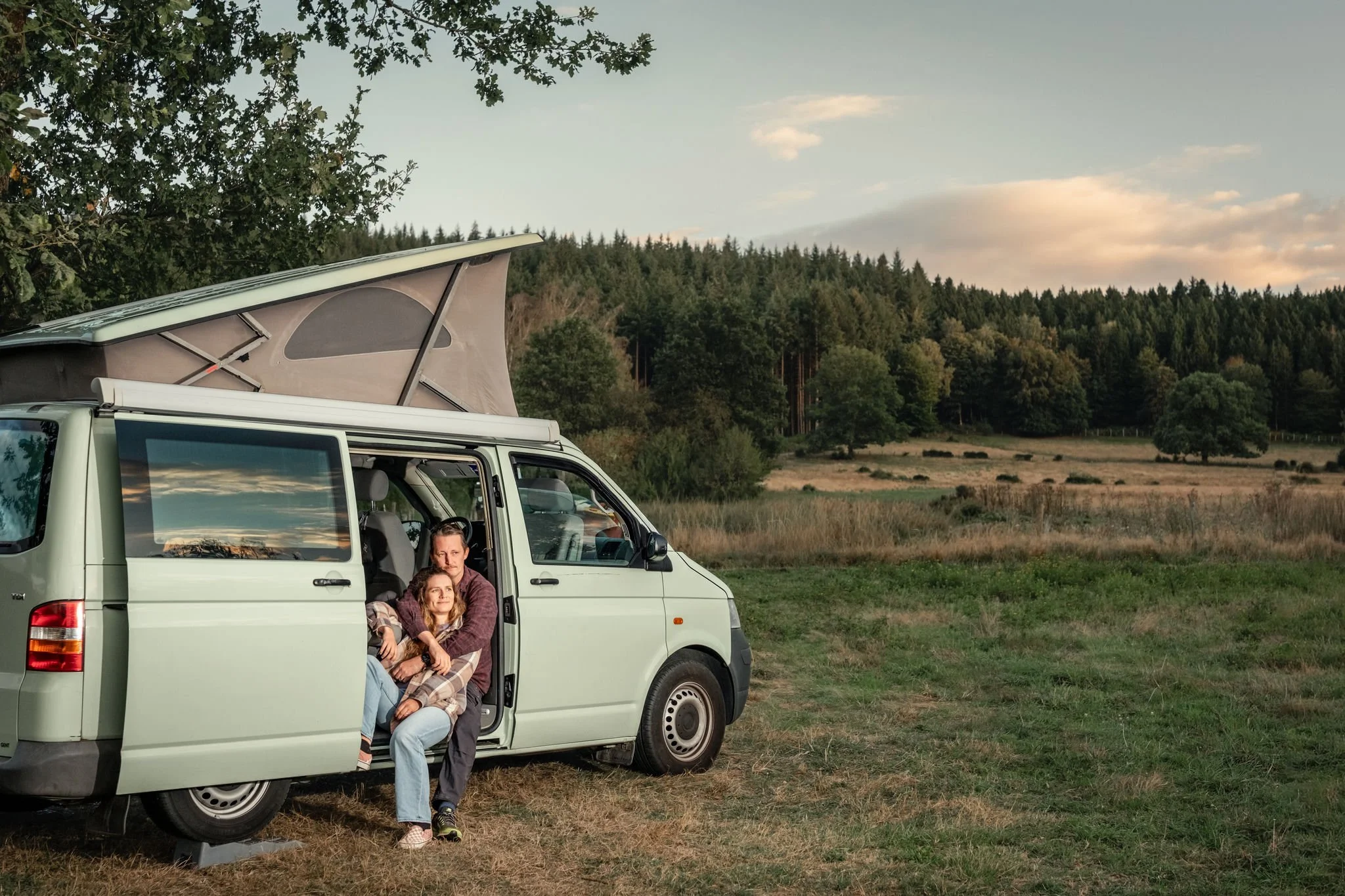 Fred et Mic, duo photographe et vidéaste de mariage, assis à la porte de leur van dans une prairie au coucher du soleil