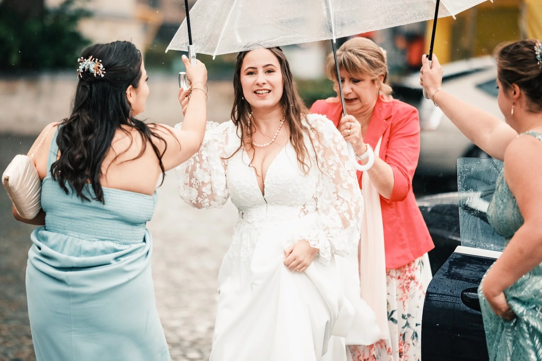 Mariée en robe à manches bouffantes sous un parapluie transparent, entourée d'invitées – mariage sous la pluie