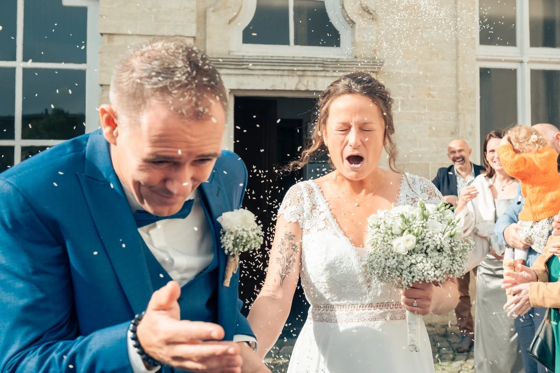 Mariés sous une pluie de riz à la sortie de la salle, la mariée émue avec son bouquet