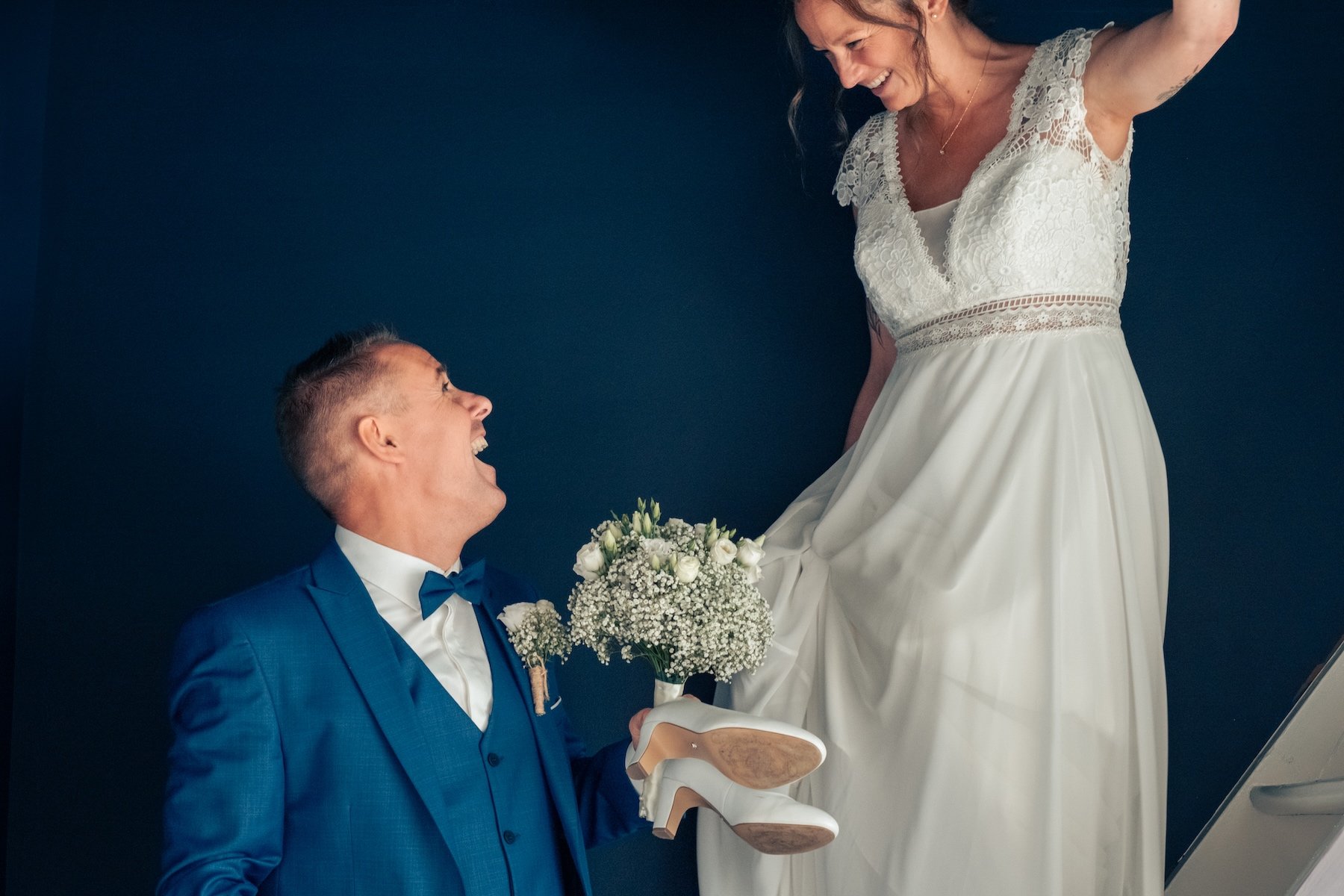Marié hilare près de sa femme en robe de dentelle, bouquet de gypsophile, sur fond bleu marine – photo de mariage