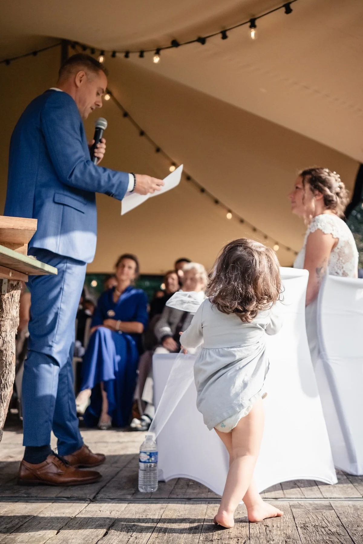 Discours au micro pendant la cérémonie sous tente, un jeune enfant traverse la scène devant la mariée