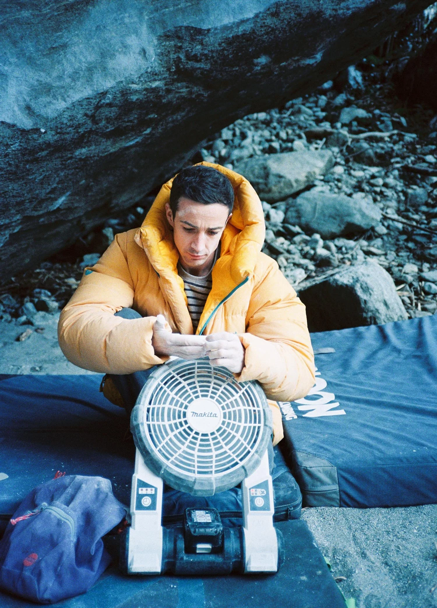 Eliot Stephens rests while trying a boulder. Here he is looking at his finger tips while cooling them with a fan.