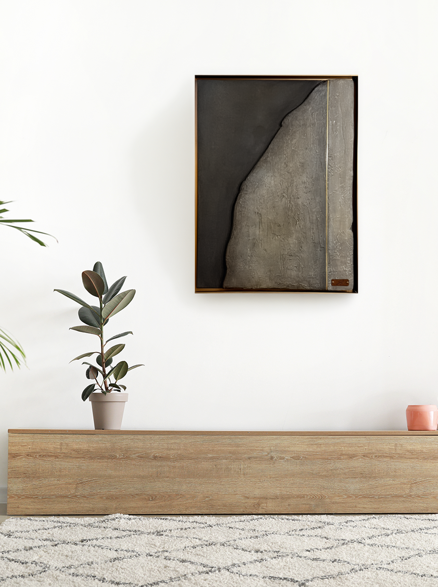 Minimalist living room with a white wall, a tall potted plant on a wooden shelf, a framed abstract art piece, and a pink vase on the shelf, with a textured rug on the floor.