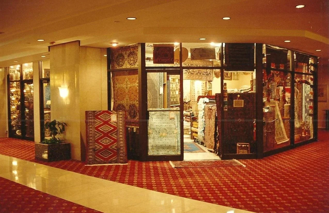 View of a carpet store inside a shopping mall, with rolls of rugs displayed inside and outside the glass storefront.