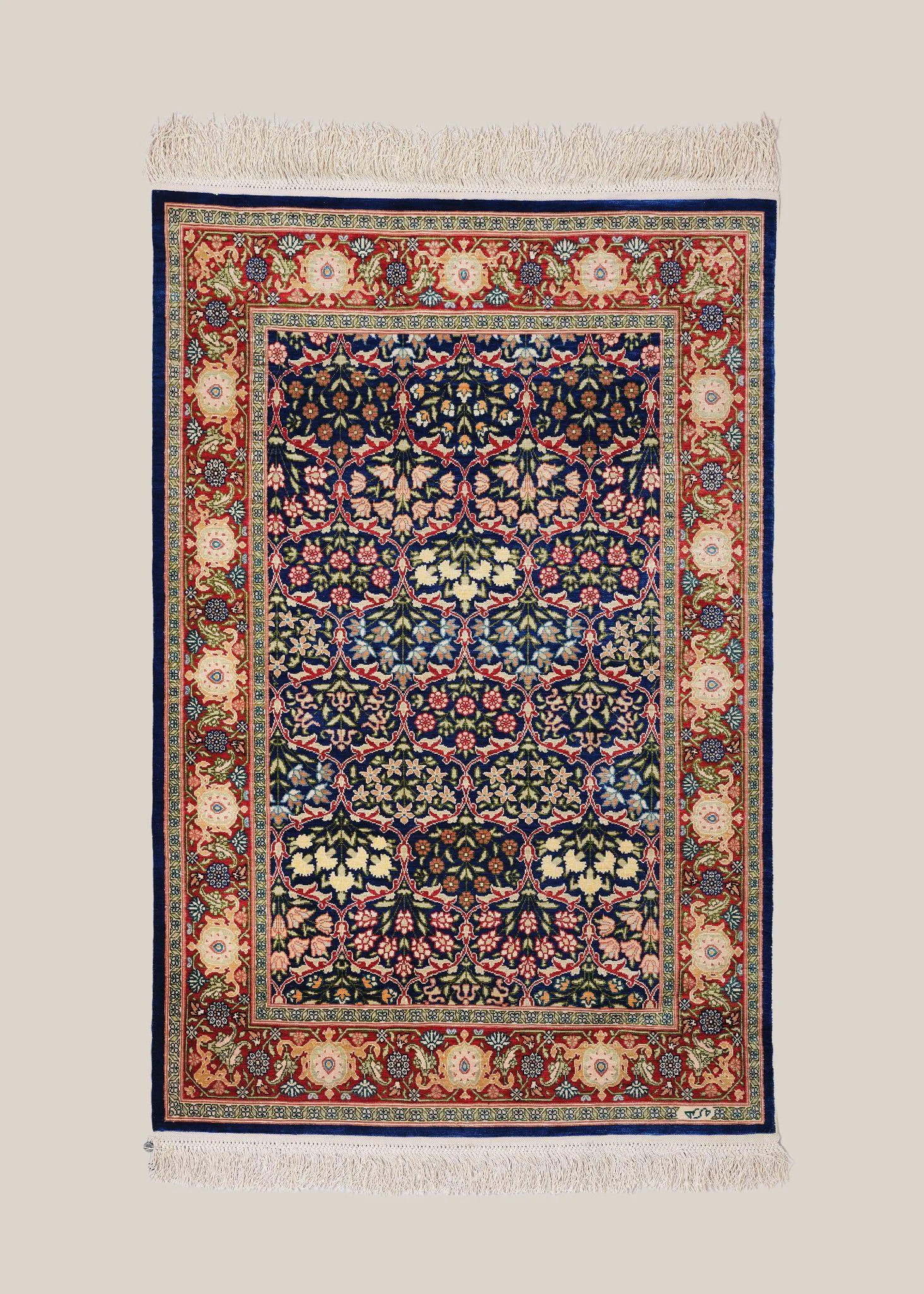 An ornate Persian-style rug with a central floral pattern in navy blue, cream, pink, and green, surrounded by a decorative border with floral motifs in similar colors.
