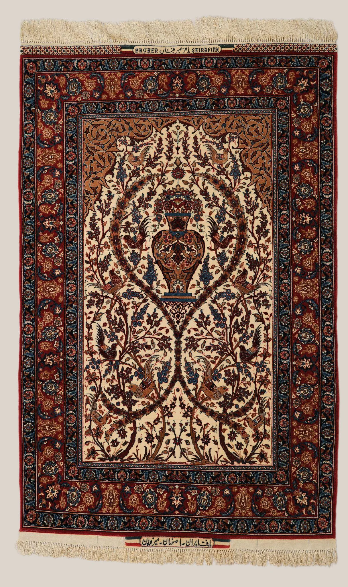 A traditional Persian rug with intricate floral and bird designs in red, beige, blue, and brown colors, featuring a central urn motif and surrounded by detailed borders. There are inscriptions in Persian script at the top and bottom edges.