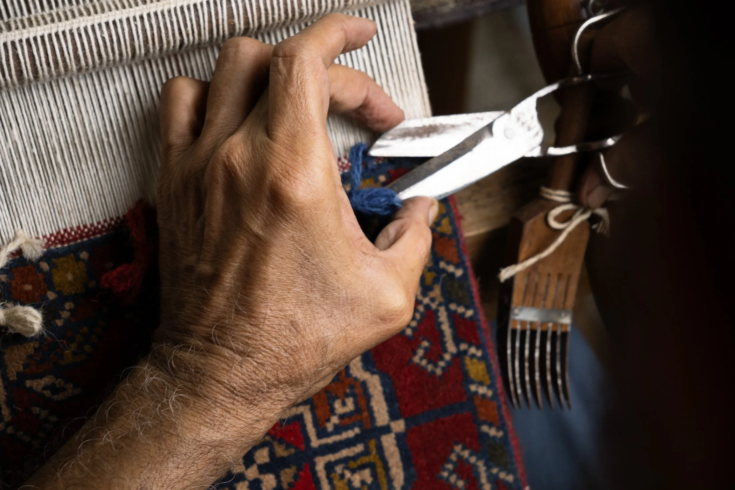 Close-up of a person's hand as they cut fabric with a large knife on a wooden surface. The fabric has a striped pattern.