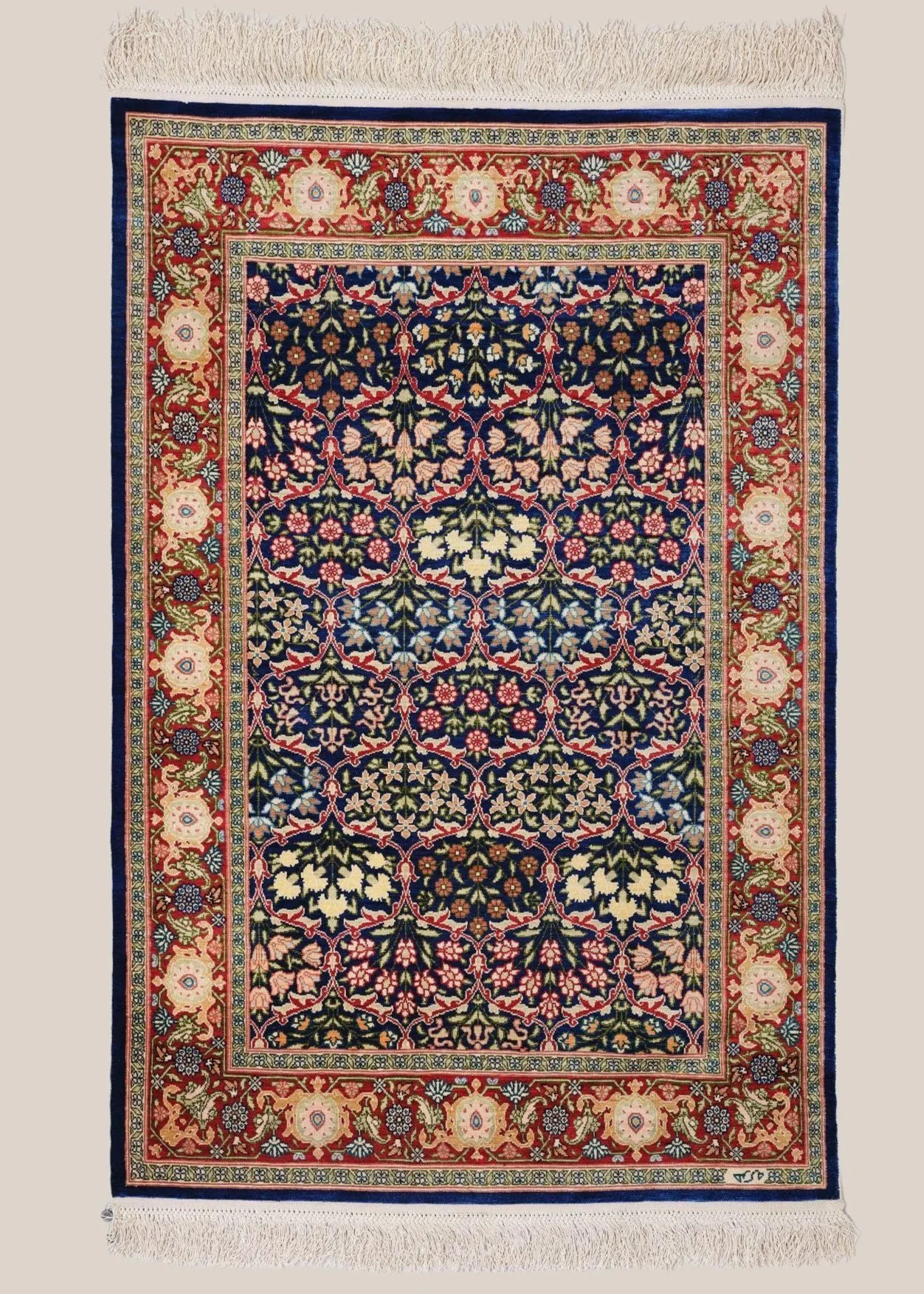 A traditional Persian-style rug with intricate floral and geometric patterns. The central area features a dark background with symmetrical floral motifs in red, pink, beige, and green. The border has a red background with large floral designs in cream, pink, and blue, framed by narrow additional borders with repeating geometric patterns. The rug has fringed edges at the top and bottom.