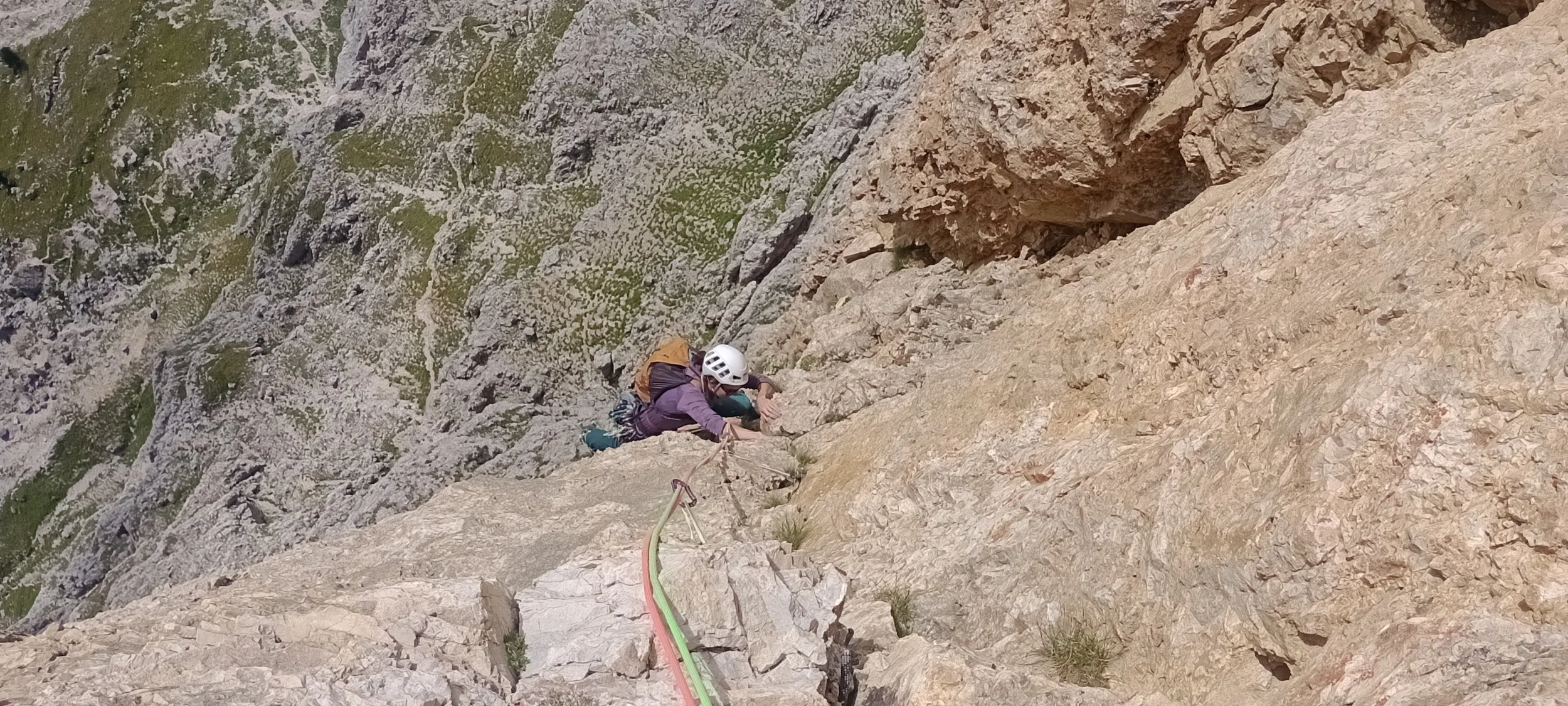 Kletterer auf einem steilen Felsanstieg in den Bergen, angebunden mit Kletterseil und mit Helm, die Kletterausrüstung trägt.
