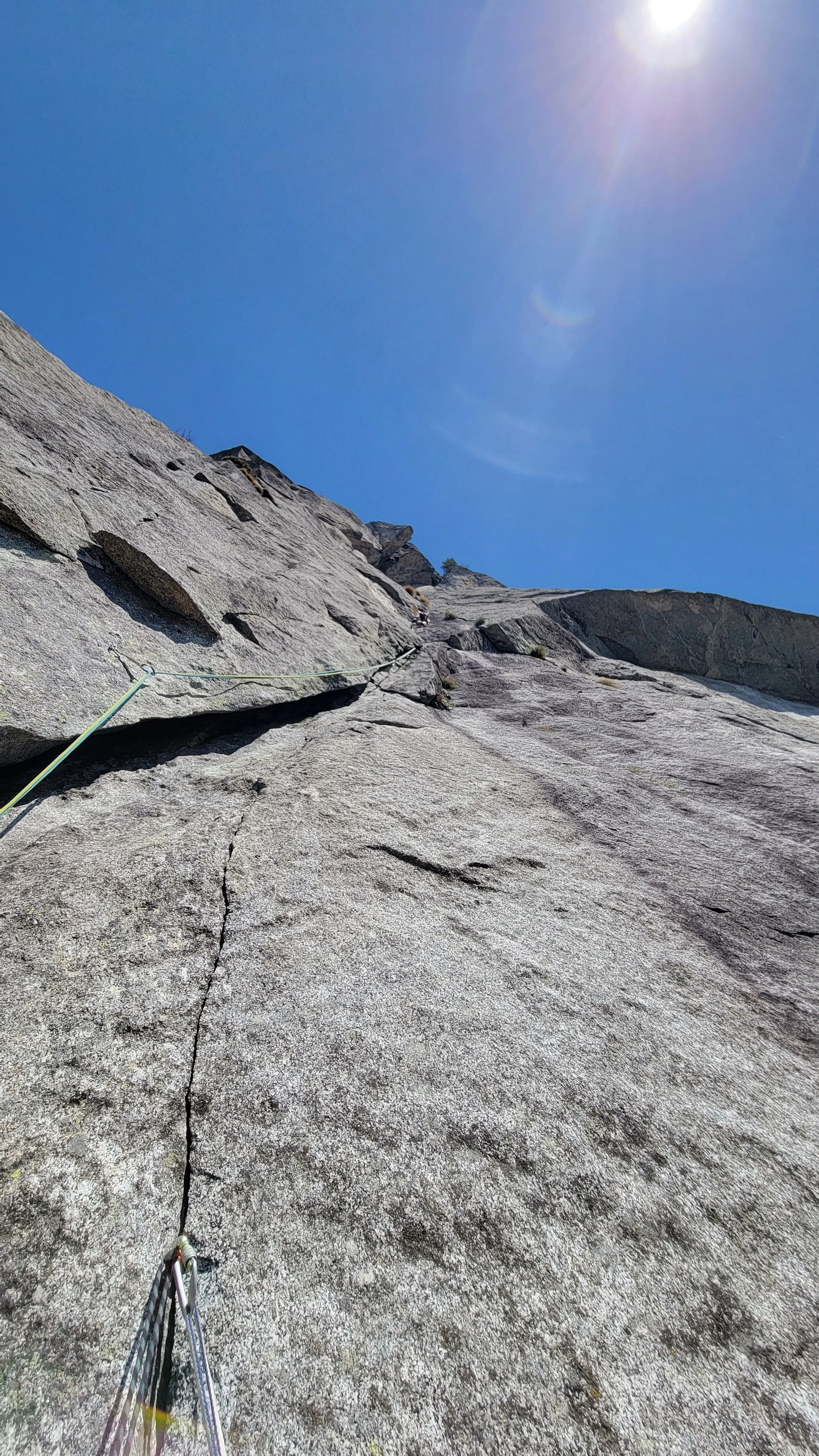 Bergkletterer klettert eine Felswand mit Kletterseil bei sonnigem Himmel.