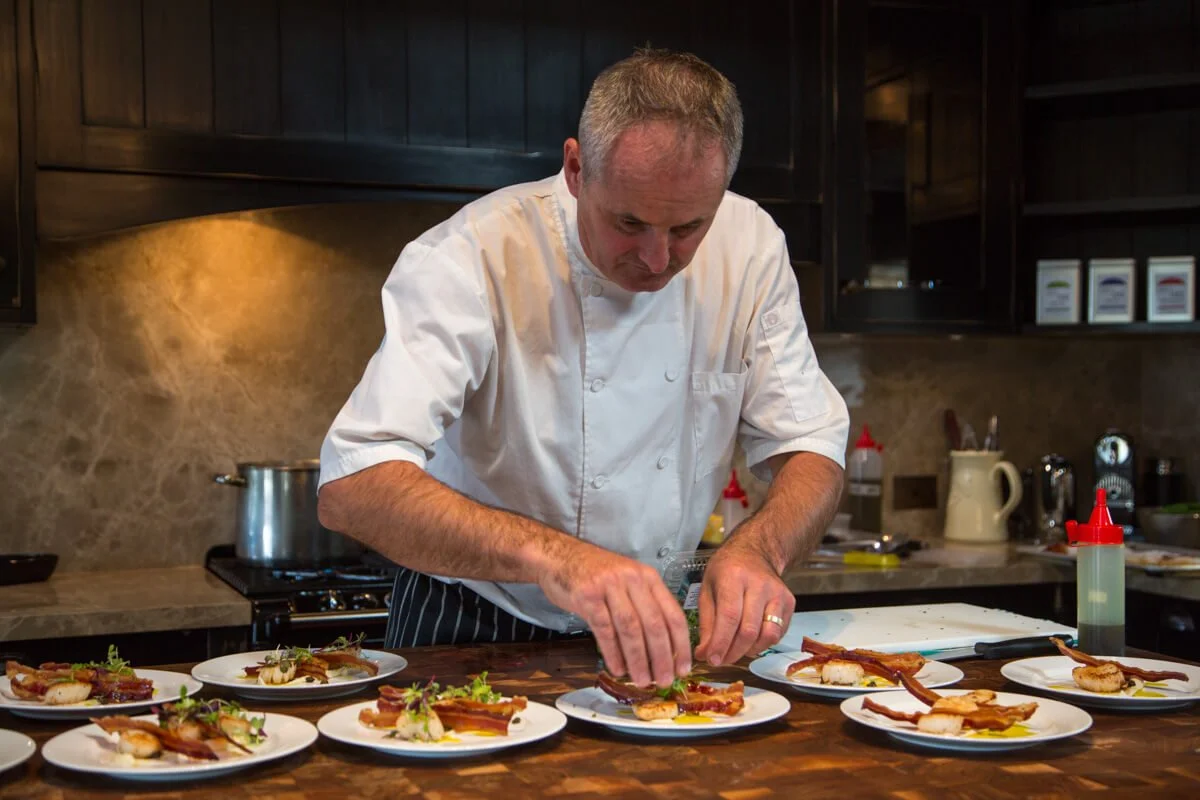 Chef garnishing multiple plates of food in a professional kitchen.