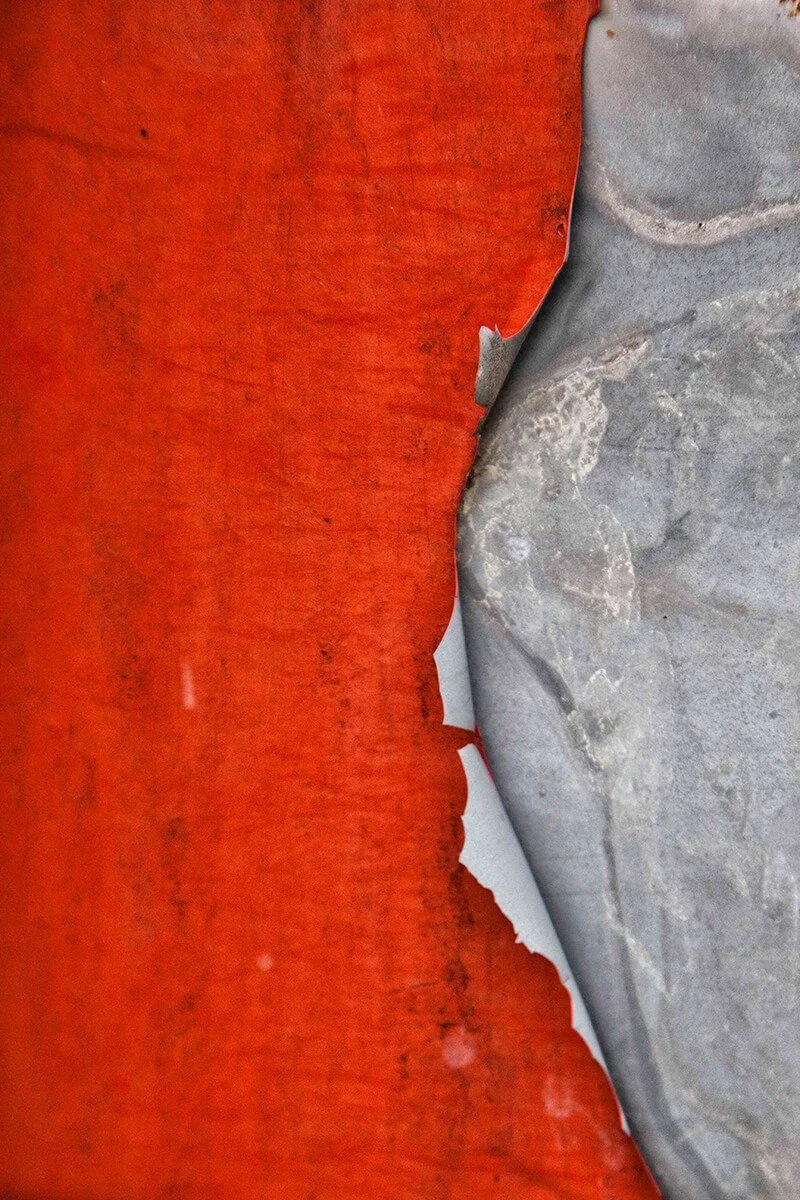 Close-up of peeling orange construction barrier with a gray surface underneath.