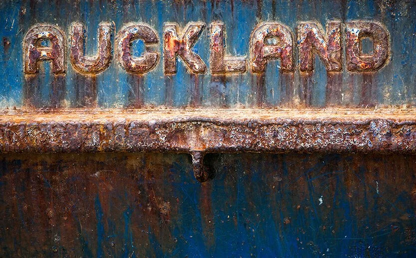Rusty metal surface with the word 'AUCKLAND' in large, weathered letters.