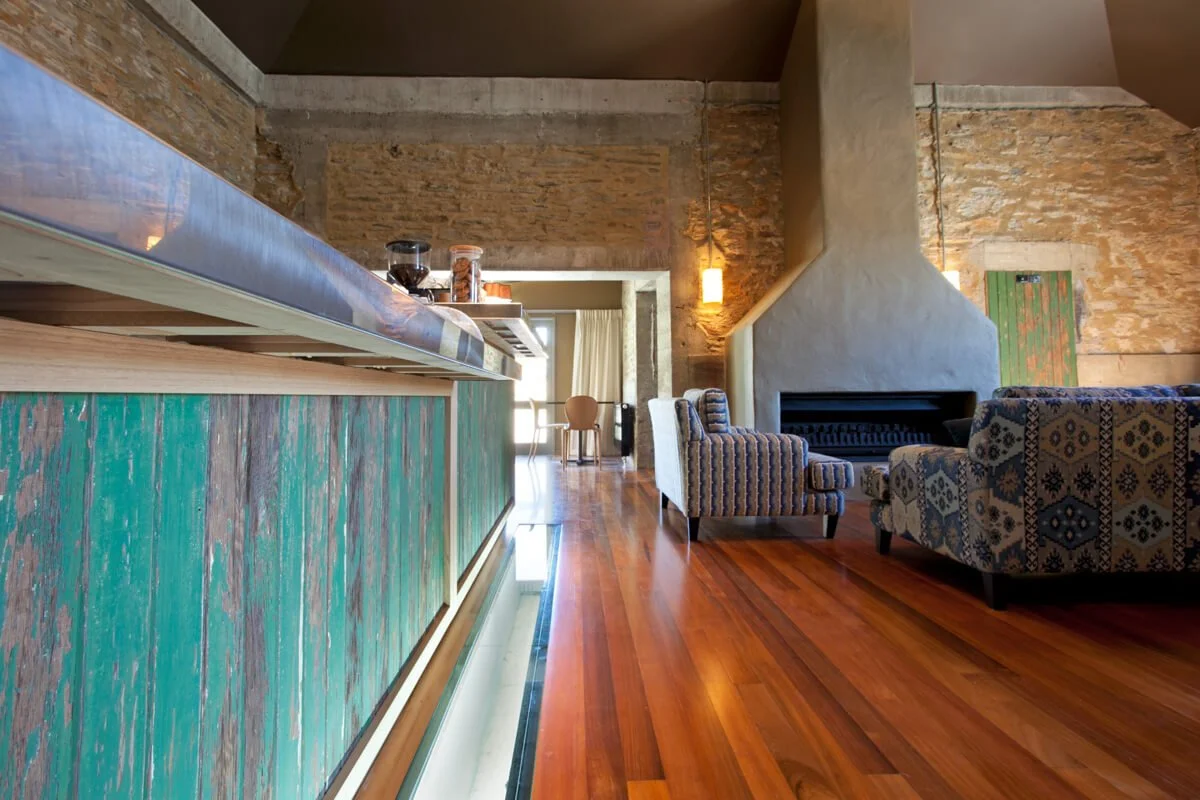 Interior of a cozy room with a fireplace, patterned armchairs, a wooden floor, and a kitchen counter with glass jars on top.