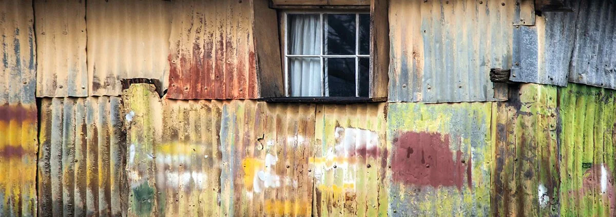 Close-up of a weathered metal wall with peeling paint and a small window.