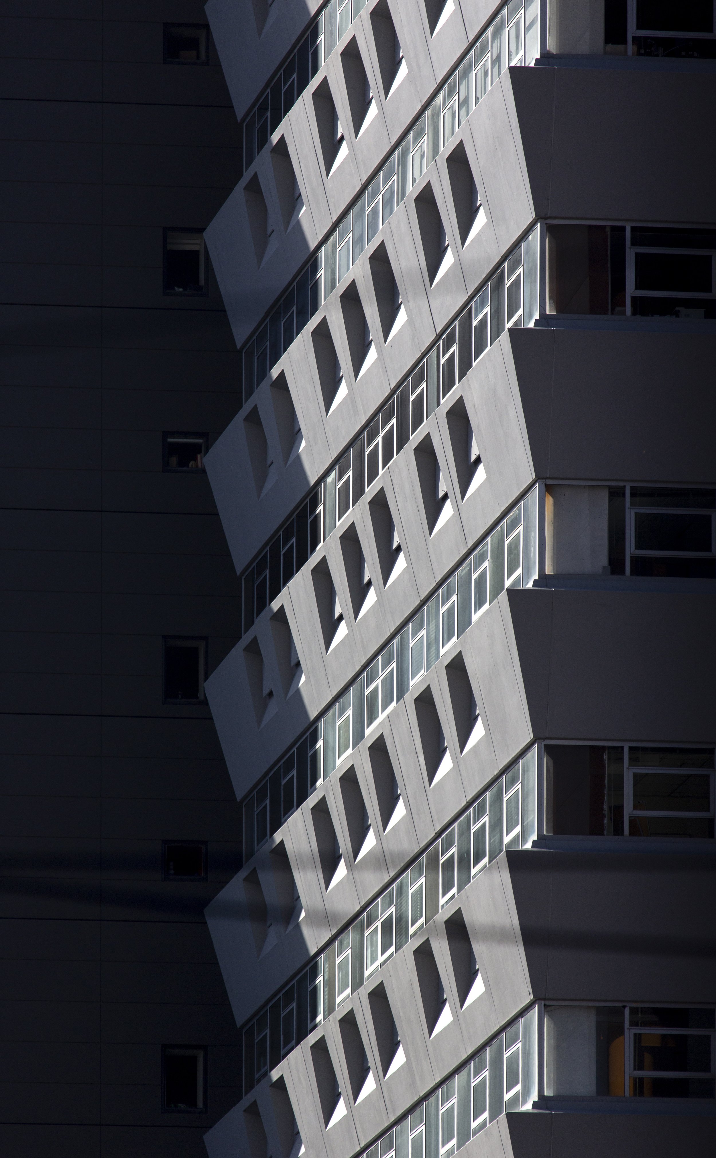 Looking up at a shaft of sun light up one face of a building between surrounding buildings