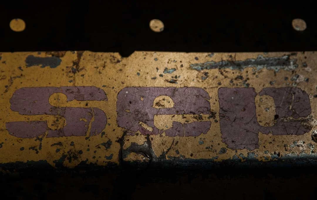 Close-up of a weathered yellow metal surface with the partially visible purple letters 'SICAL' on it, showing peeling paint and signs of rust.