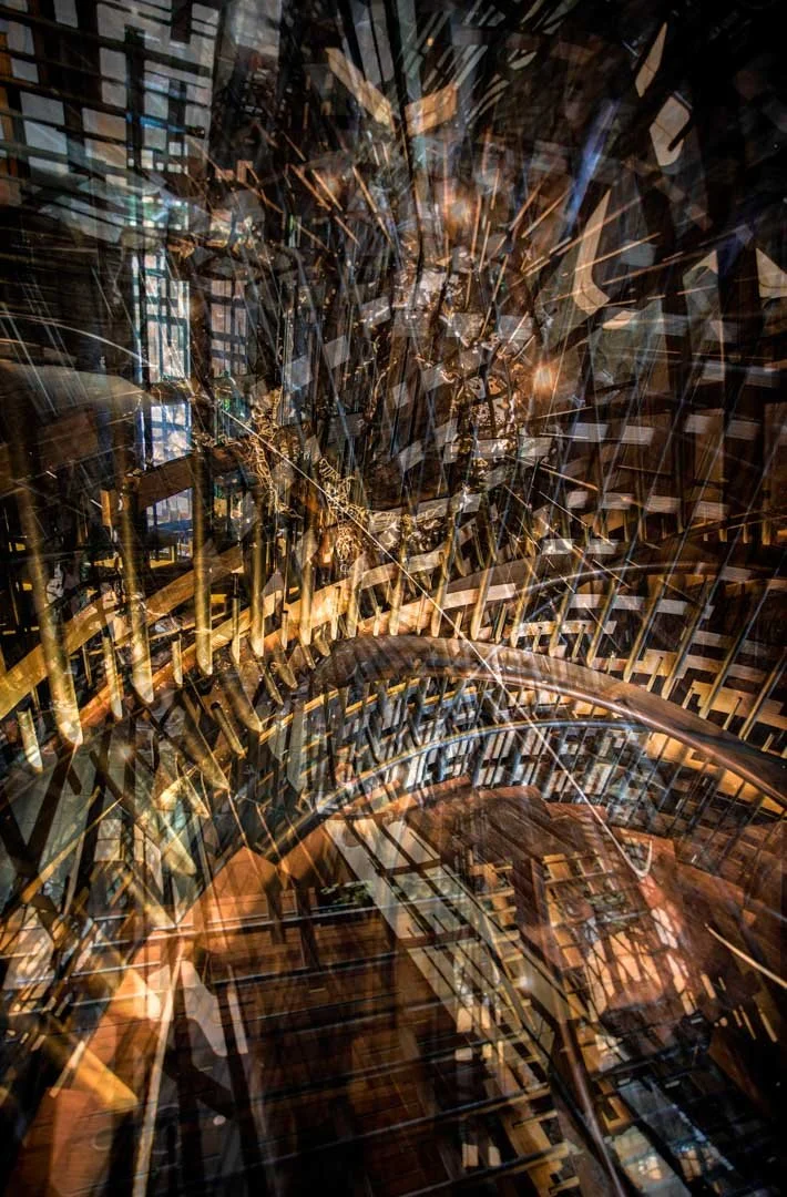 An abstract, layered photo of a modern, glass and metal architectural interior with a spiral staircase and multiple reflections.