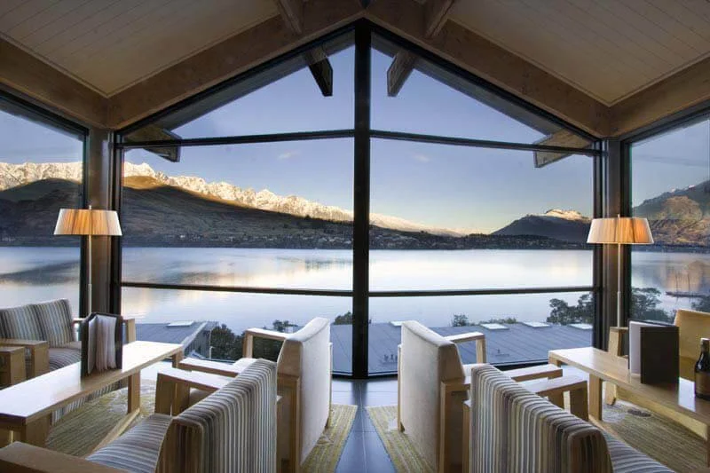 Interior of a cozy lakeside restaurant with large windows showing mountains and reflections on the water.