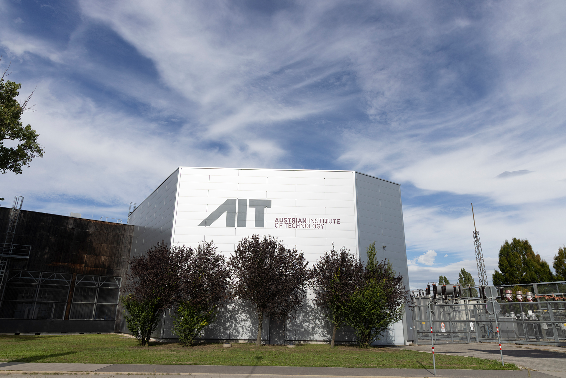 The AIT building with the AIT logo behin a row of trees.