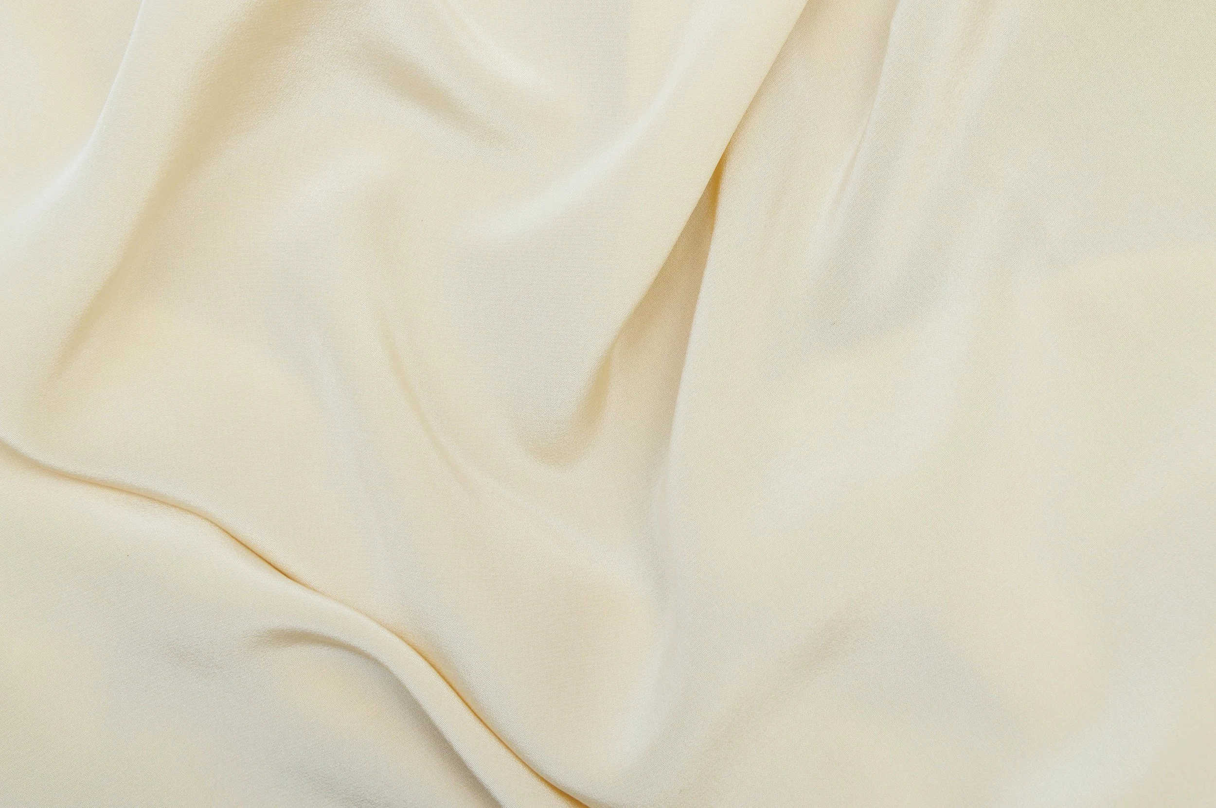 Close-up view of cream-colored silky satin fabric with soft folds and smooth texture.