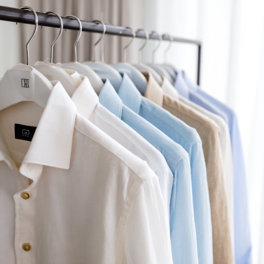 A row of neatly hanging shirts in white, blue, beige, and light blue on a clothing rack.