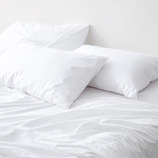 Bed with white sheets and two white pillows against a white wall.