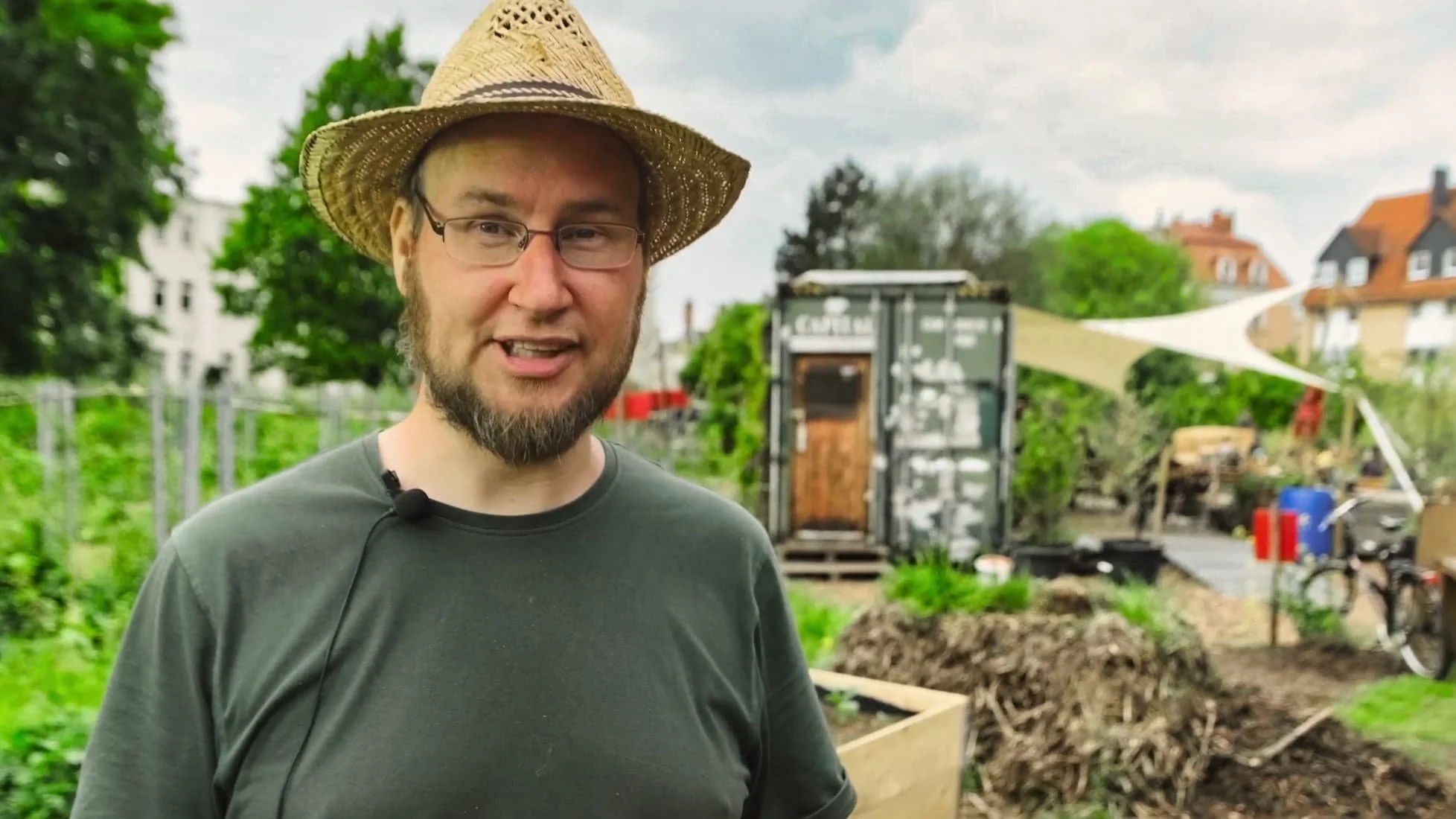 Mann in Hut steht im Garten mit Pflanzbeeten und Gartenmöbeln.