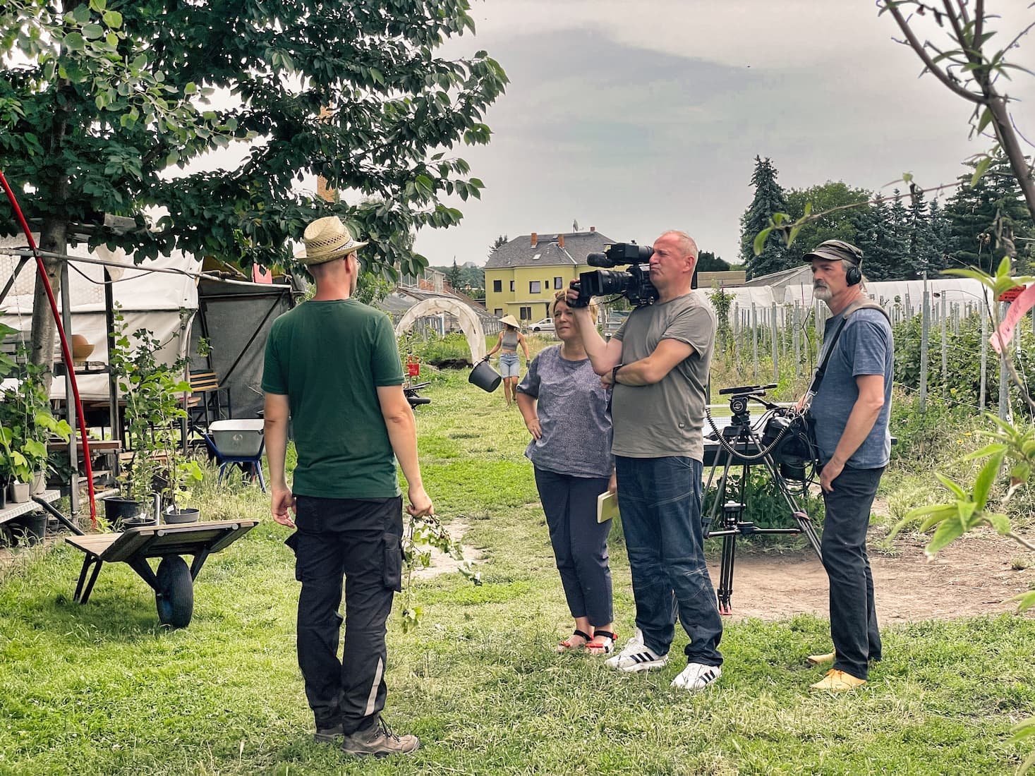 Menschen filmen und interviewen eine Frau in einem Garten mit Pflanzen und Zelten.