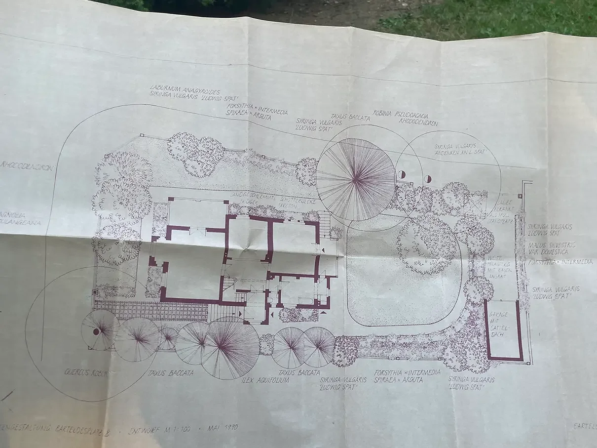 Detaillierter Garten- und Hausplan mit Bäumen, Sträuchern und Gehwegen, handgezeichnet, mit Beschriftungen in deutscher Sprache.