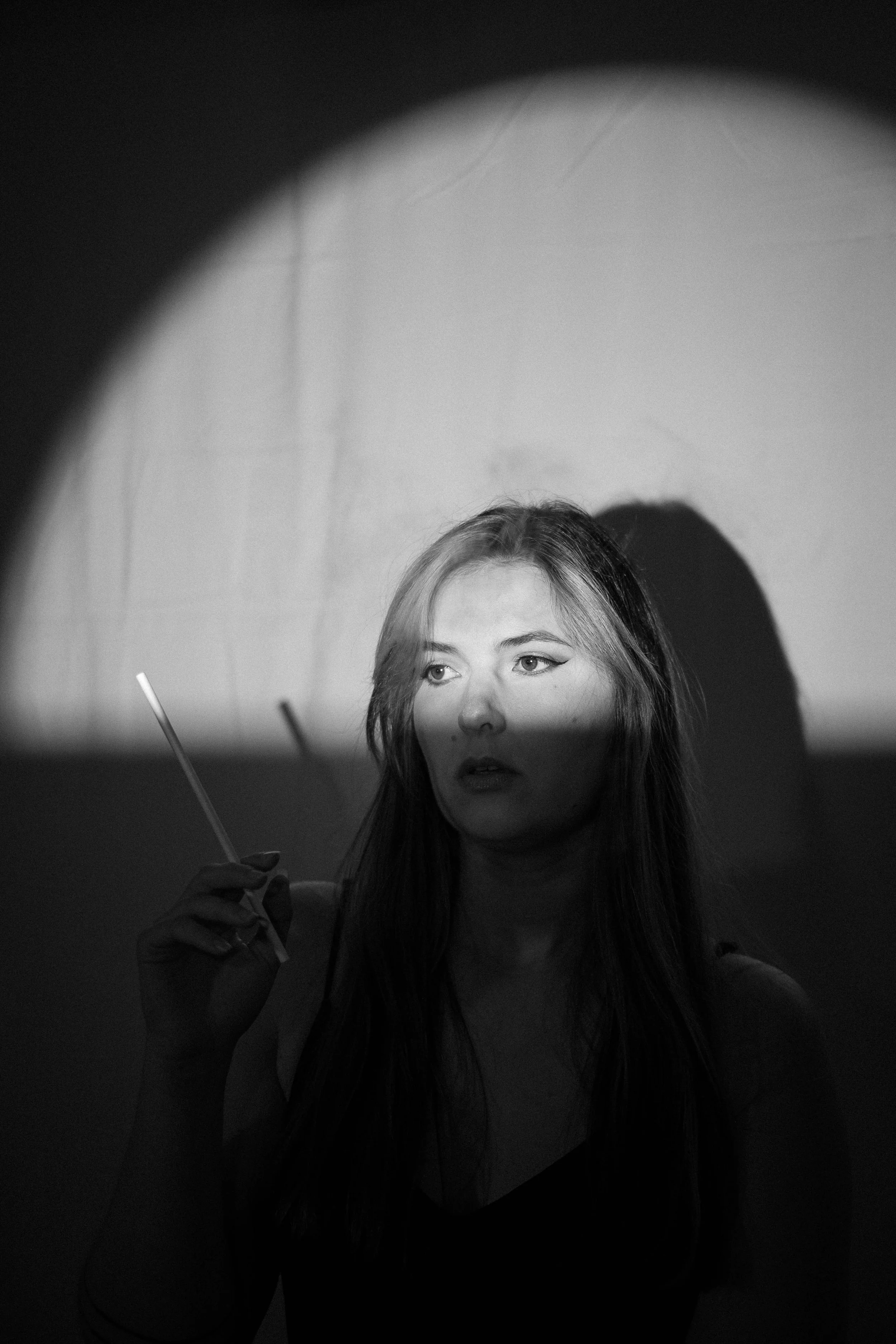 Une jeune femme avec des cheveux longs, tenant un bâton lumineux, illuminée par un faisceau de lumière dans un environnement sombre.
