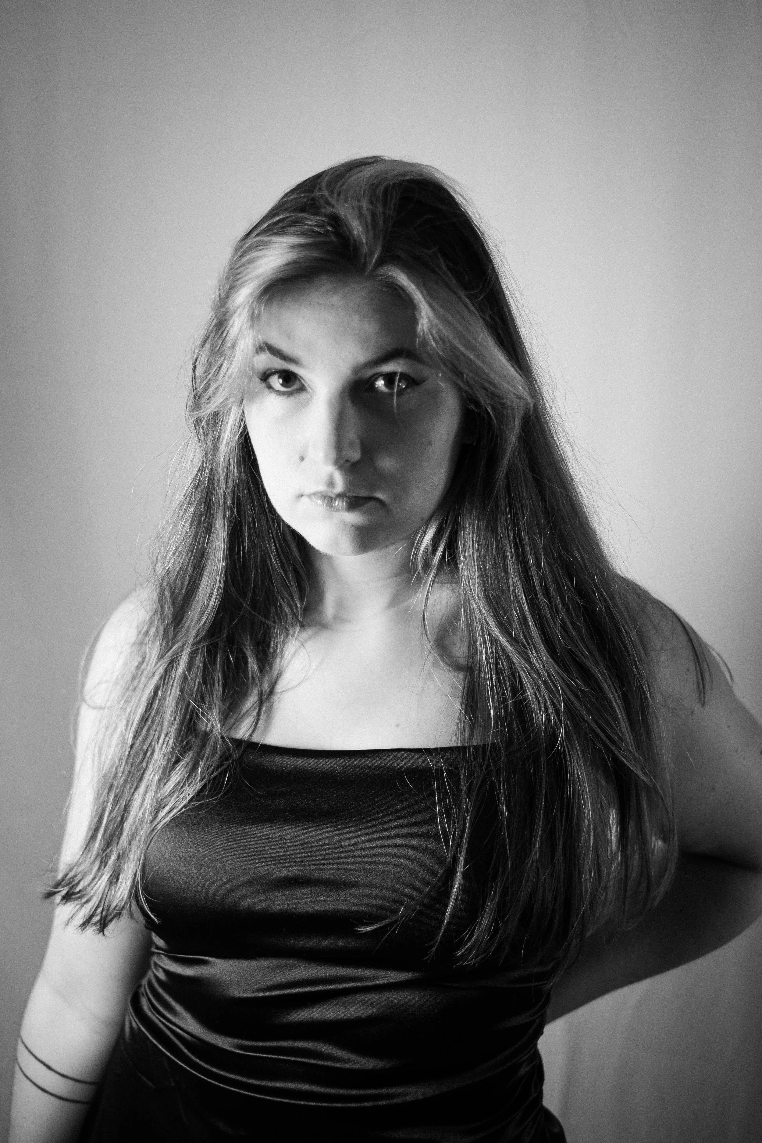 Un portrait en noir et blanc d'une femme avec de longs cheveux, portant un haut satiné, regardant directement l'appareil.