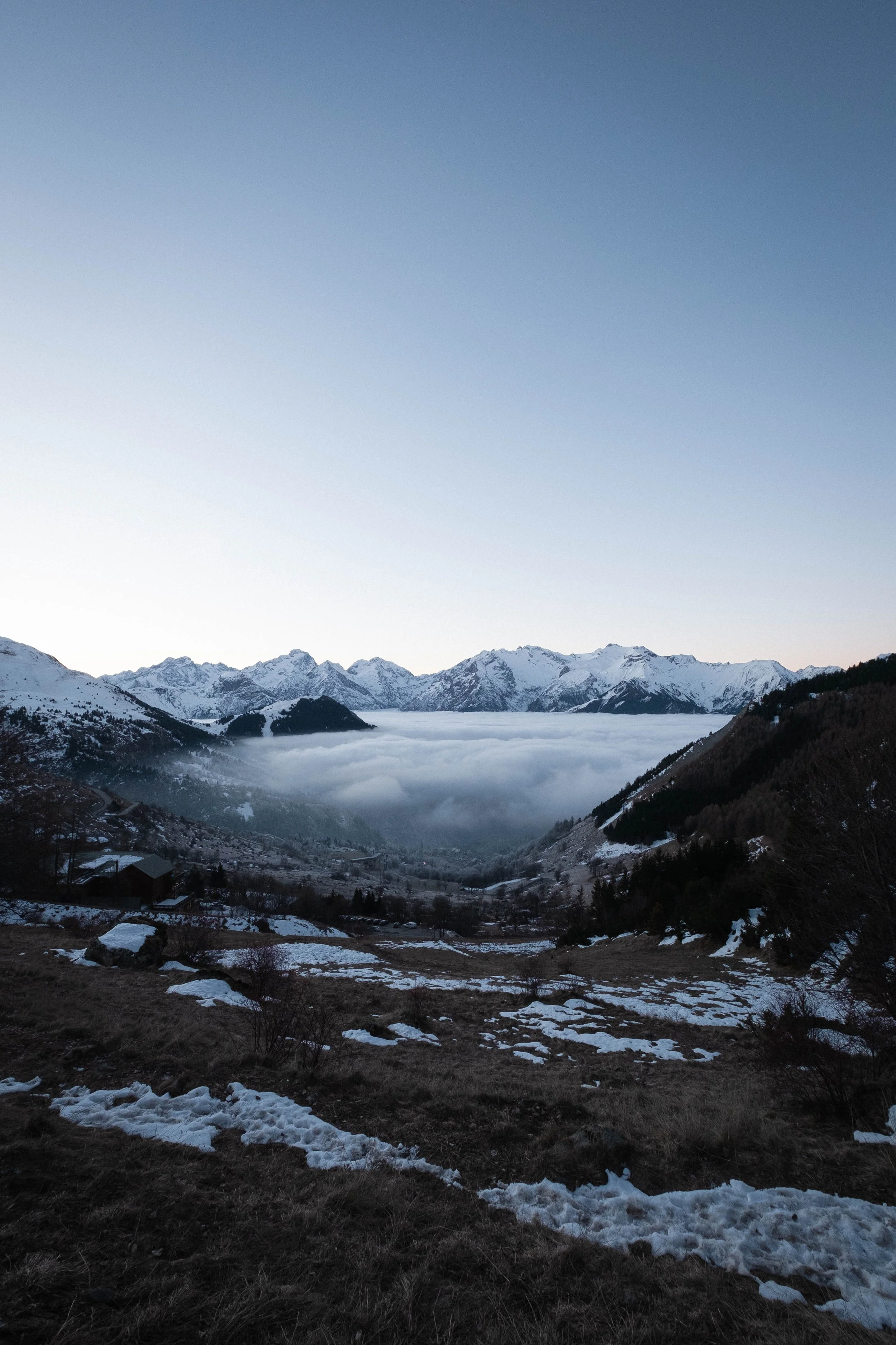 Paysage de montagne enneigée avec des sommets, des nuages en bas et un ciel clair.