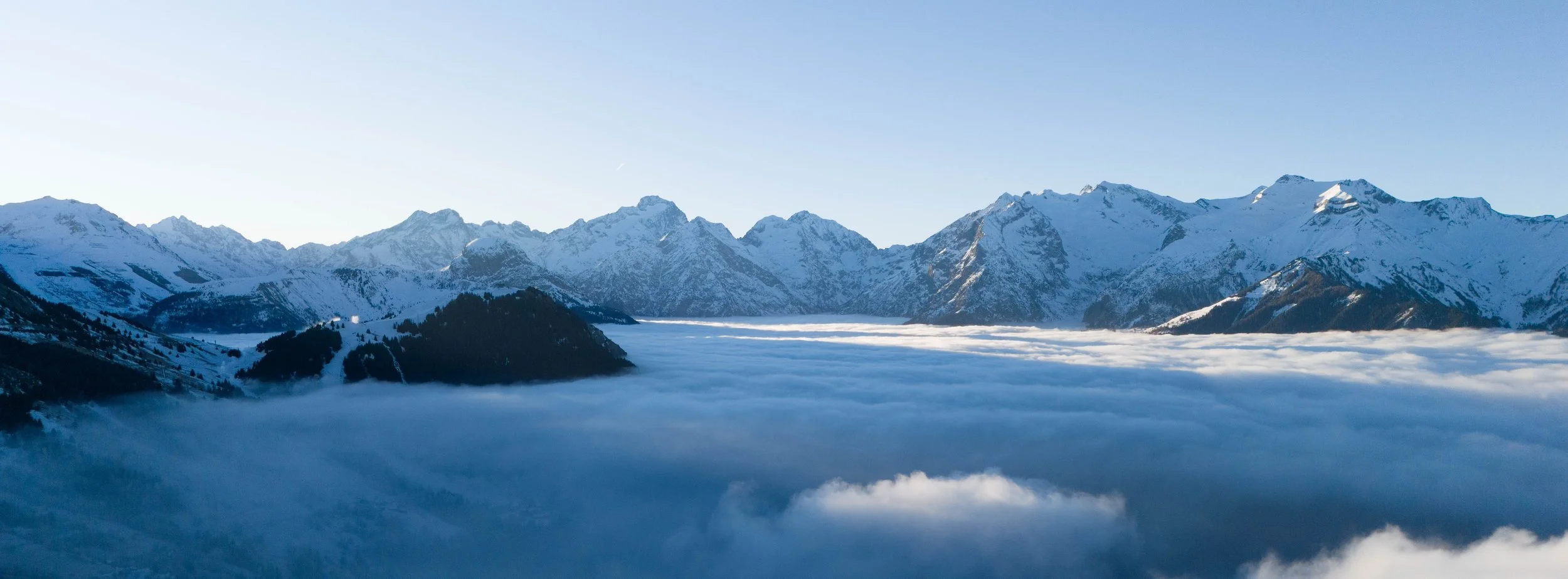 Montagnes enneigées au-dessus d'une mer de nuages bleus, sous un ciel clair.