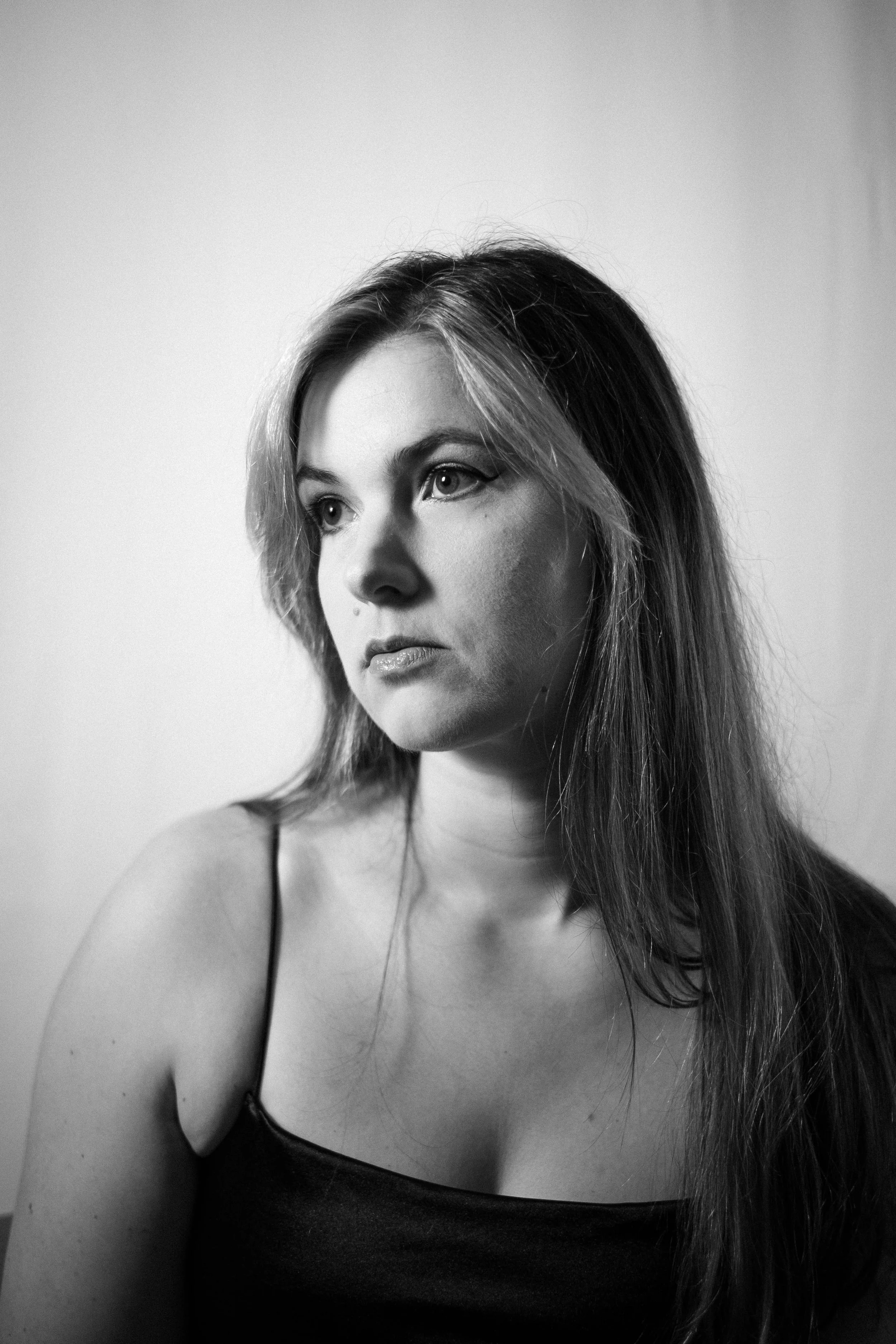 Portrait en noir et blanc d'une femme aux cheveux longs et droits, portant un débardeur noir, regardant vers la gauche avec expression sérieuse.