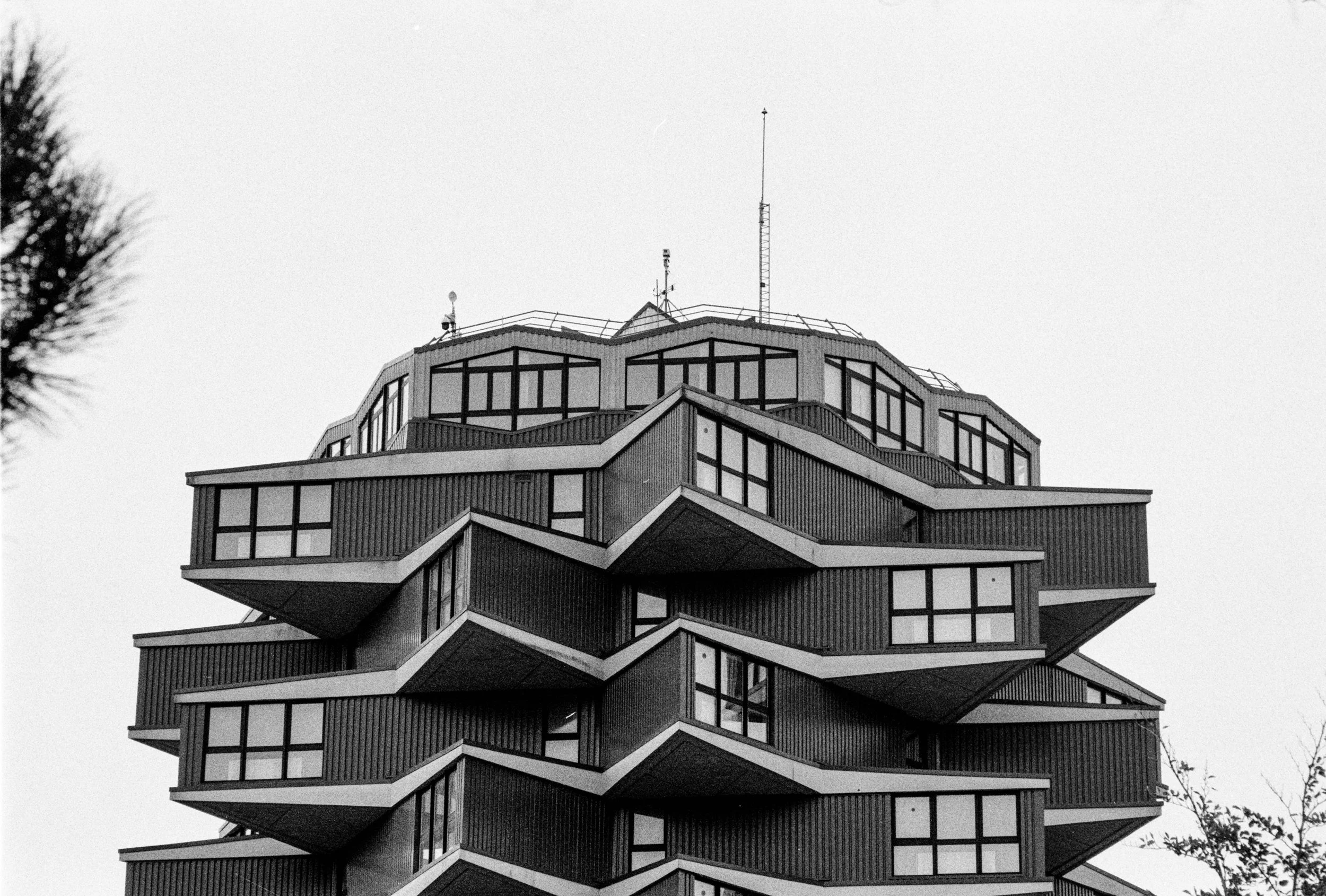 Un bâtiment résidentiel moderne avec des balcons en zigzag design, plusieurs fenêtres, et des antennes sur le toit, capturé en noir et blanc.