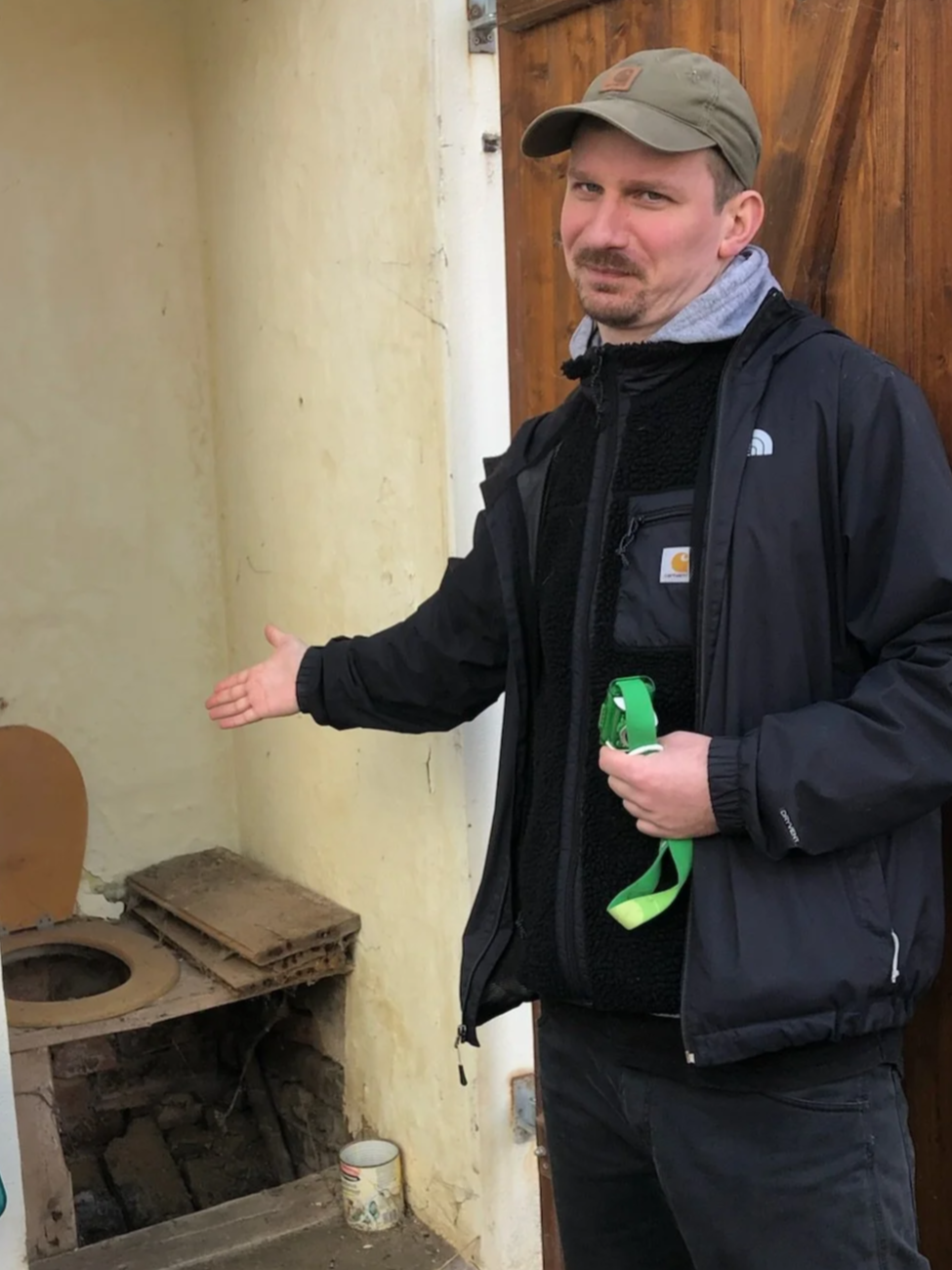 Ein Mann zeigt auf eine alte, kaputte Toilette in einem Raum mit abgenutzten Wänden.