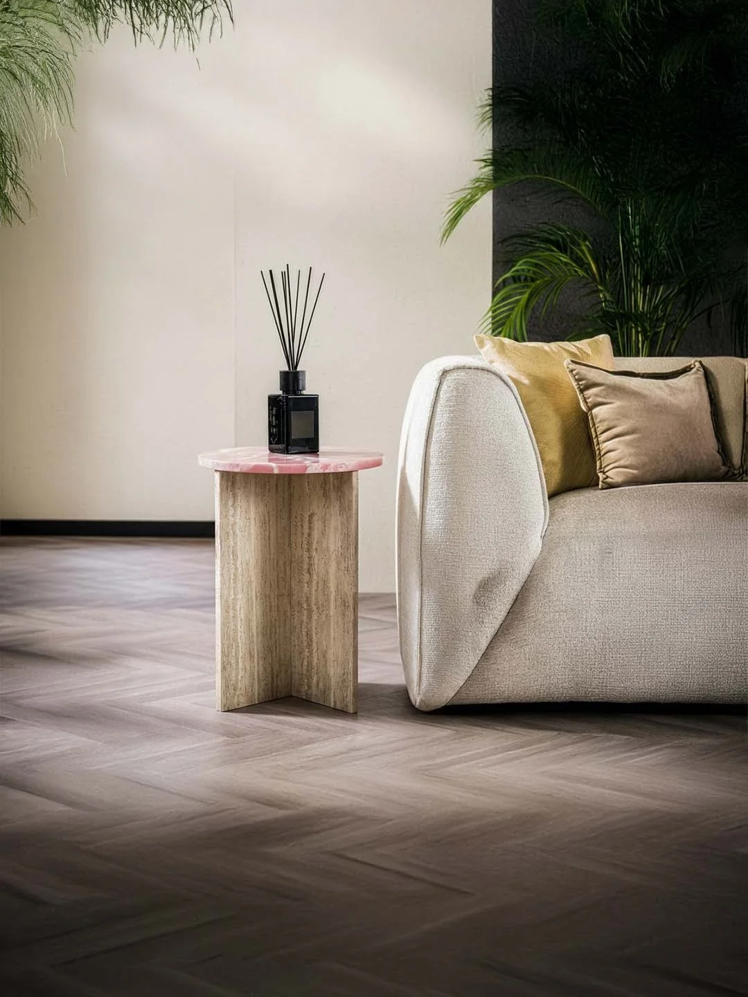 Coin salon avec canapé beige, coussins dorés et marron, table d'appoint en bois clair, plantes vertes, mur beige et noir.
