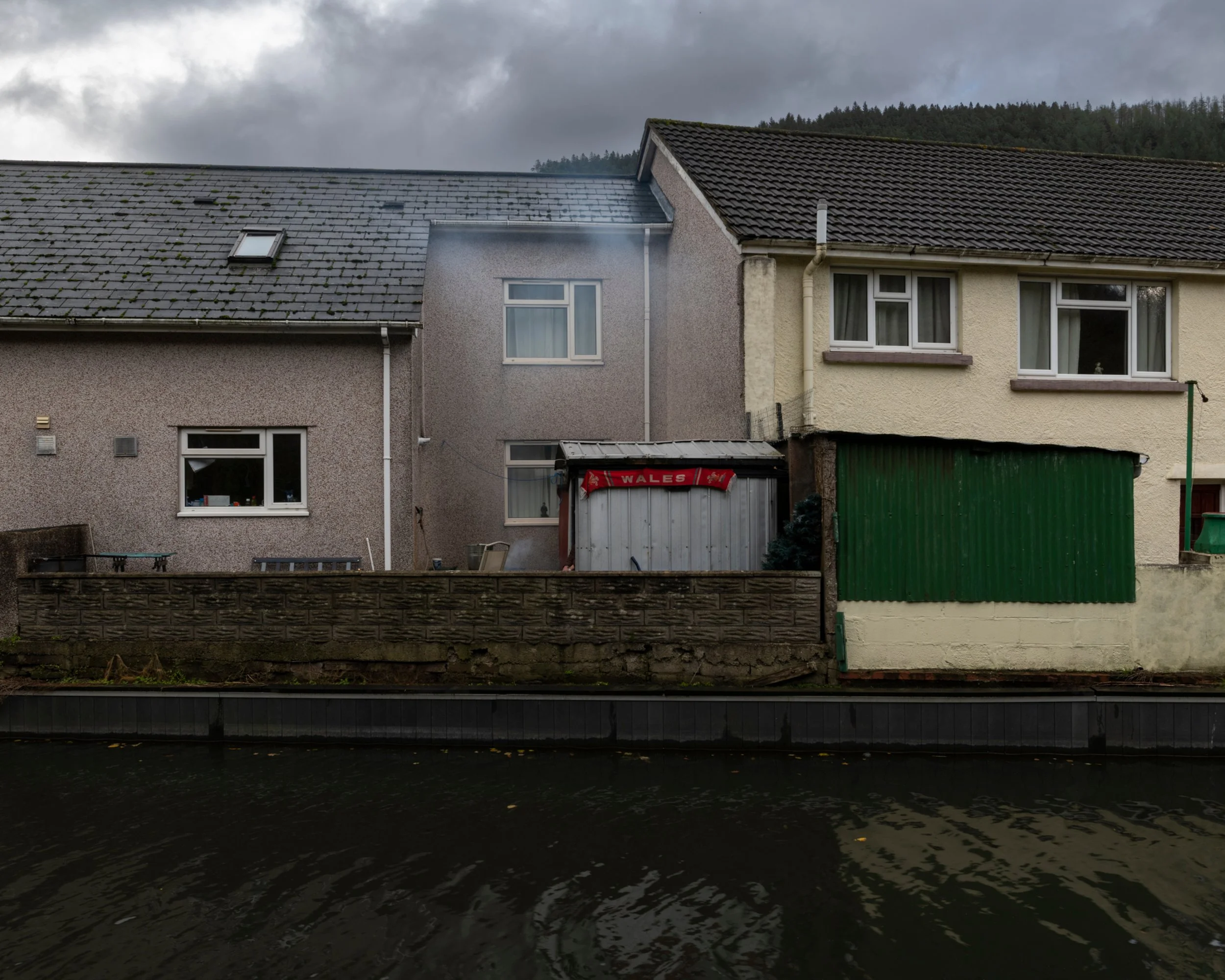 Photo of a row of houses taken from across a canal under a cloudy sky.