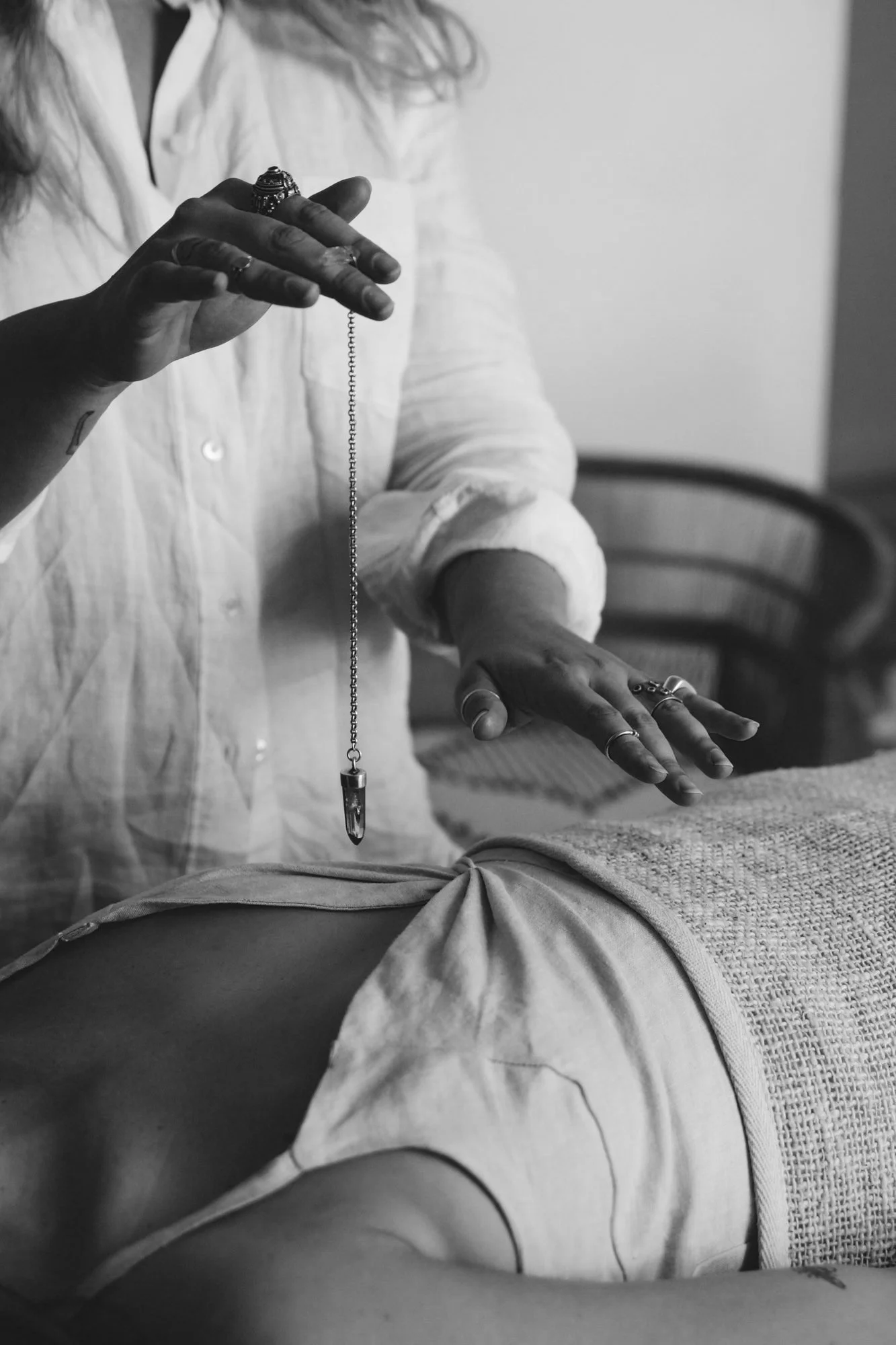A person holding a pendant necklace above a person lying down, in black and white.