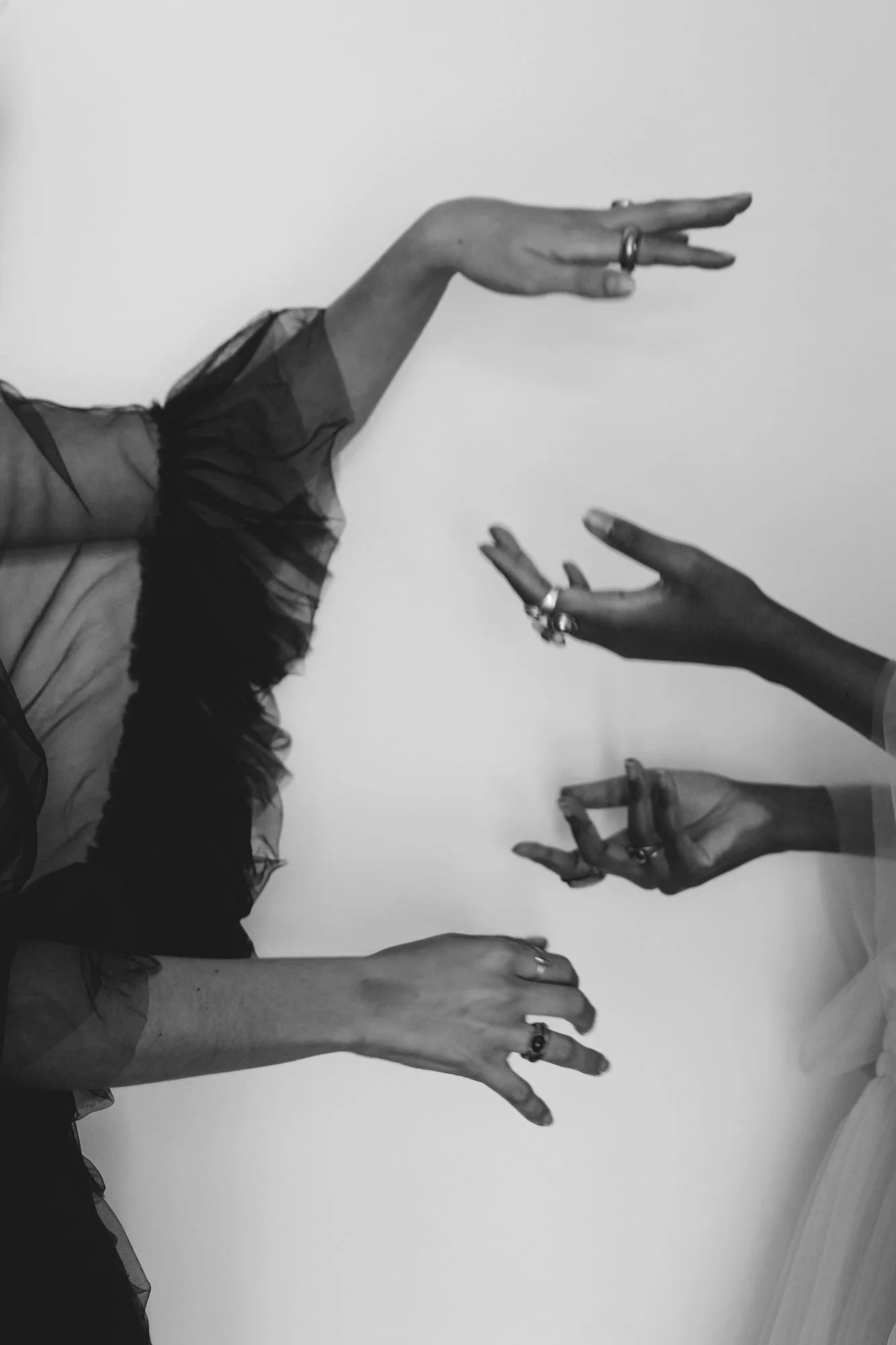 Black and white photo of four hands with rings making various gestures against a plain background.