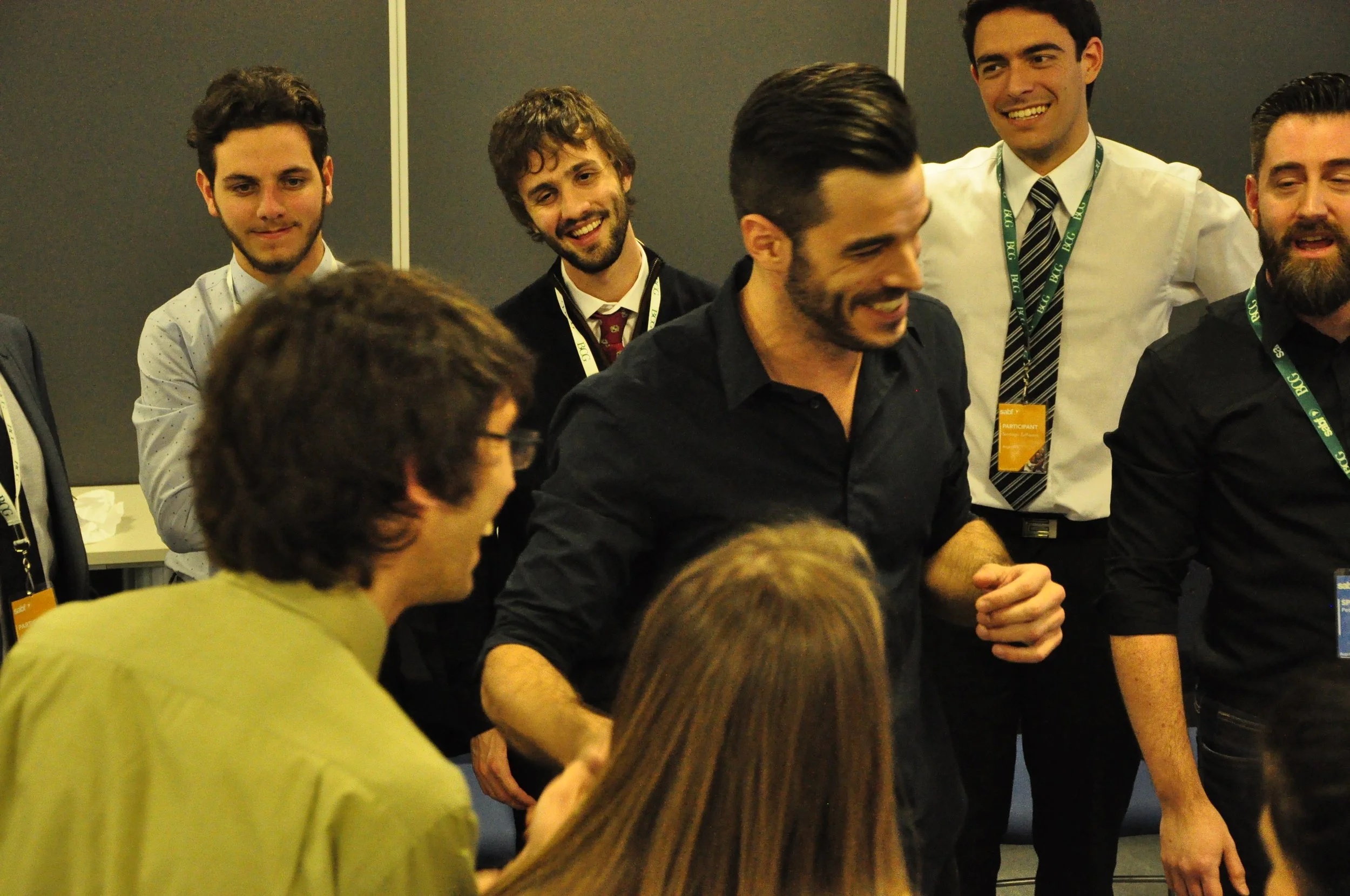 Grupo de personas en una reunión o evento, conversando, algunos sonriendo y otros atentos.