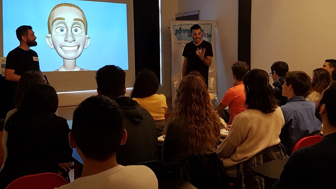 Personas en una conferencia o taller, con una presentación en una pantalla que muestra un emoji de rostro feliz con expresión nerviosa o nerviosa, en un ambiente de aula o sala de reuniones.